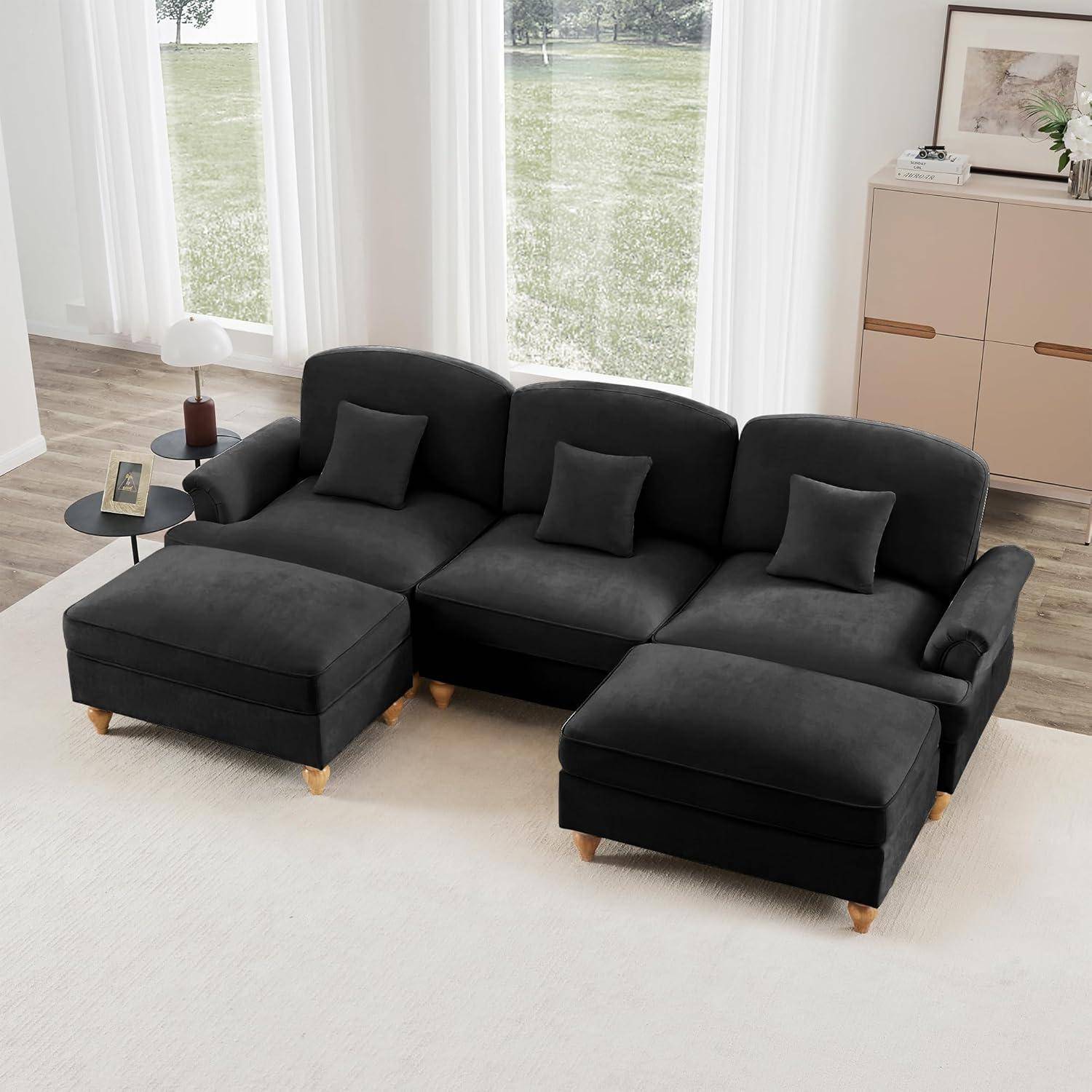 Schwarzes Ecksofa mit Chaiselongue und zwei Ottomanen in einem hellen Wohnzimmer, mit drei Dekokissen und Beistelltischen neben großen Fenstern.