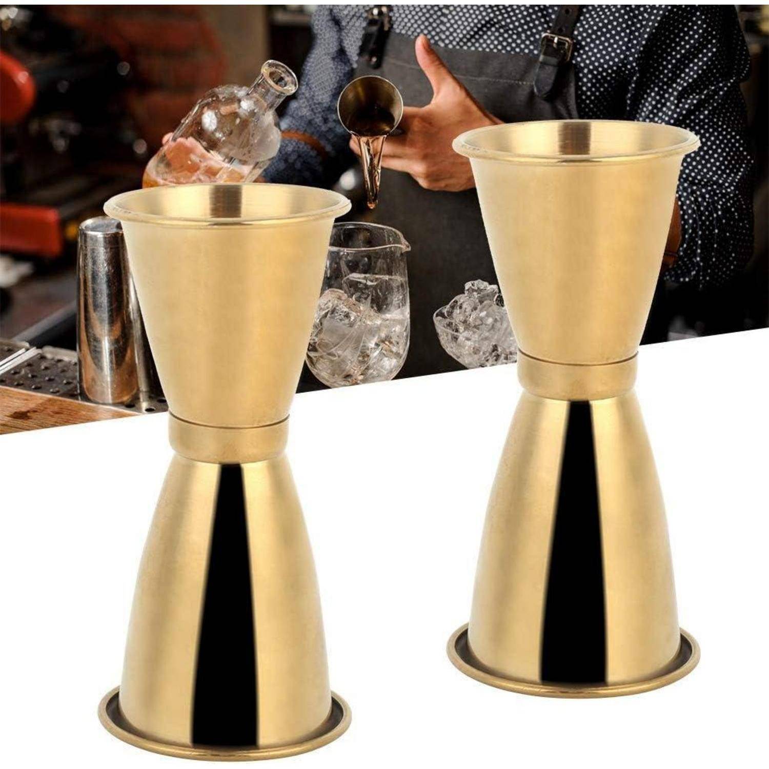 Zwei goldene Cocktail-Messbecher auf einer Bartheke, im Hintergrund ein Barkeeper, der Flüssigkeit eingießt.