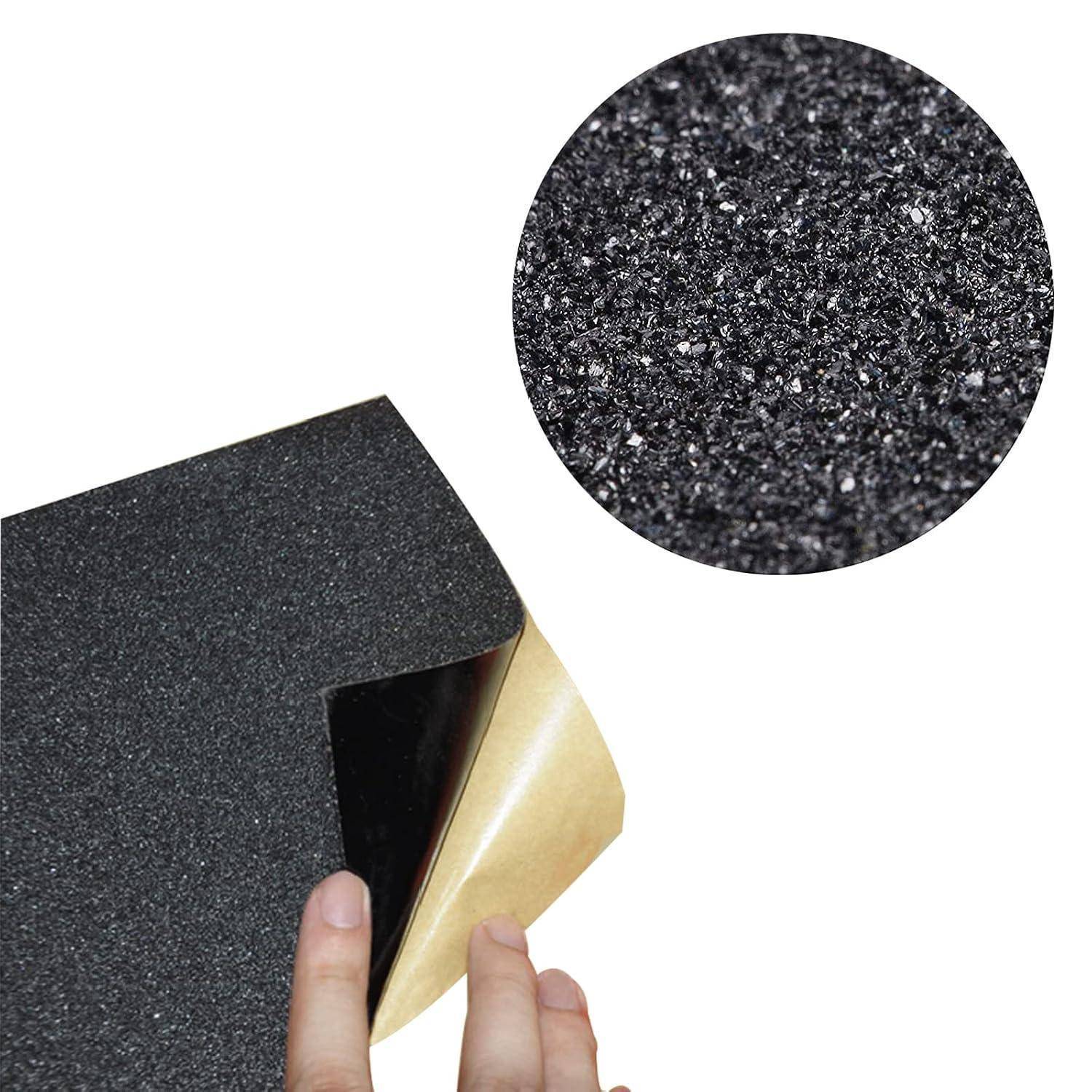 Hand zieht klebstoffbeschichtetes schwarzes Schleifpapier zurück und zeigt die strukturierte Körnung und hellbraune Papierrückseite; Ausschnitt vergrößert die Schleiffläche.