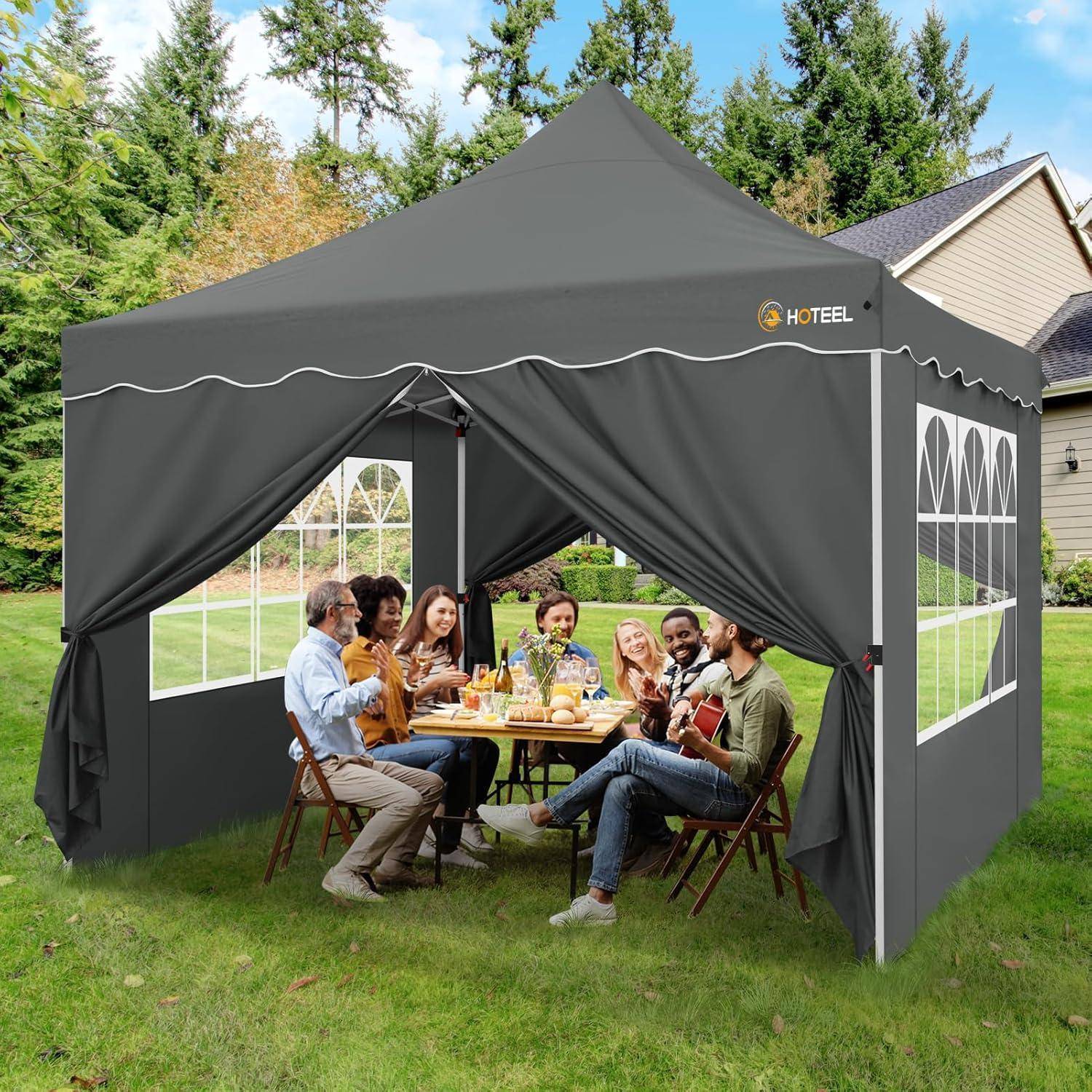 Menschen, die an einem Tisch in einem großen grauen Popup-Baldachzelt im Hinterhof speisen und sich unterhalten, mit offenen Seitengardinen und Fensterpanelen.