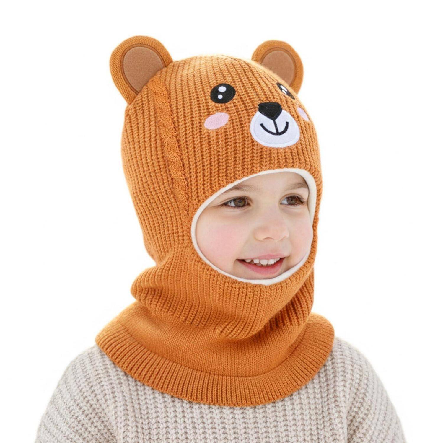 Kind mit einer orangefarbenen gestrickten Bärenmütze mit Gesichtsöffnung, lächelnd vor einem einfachen weißen Hintergrund.
