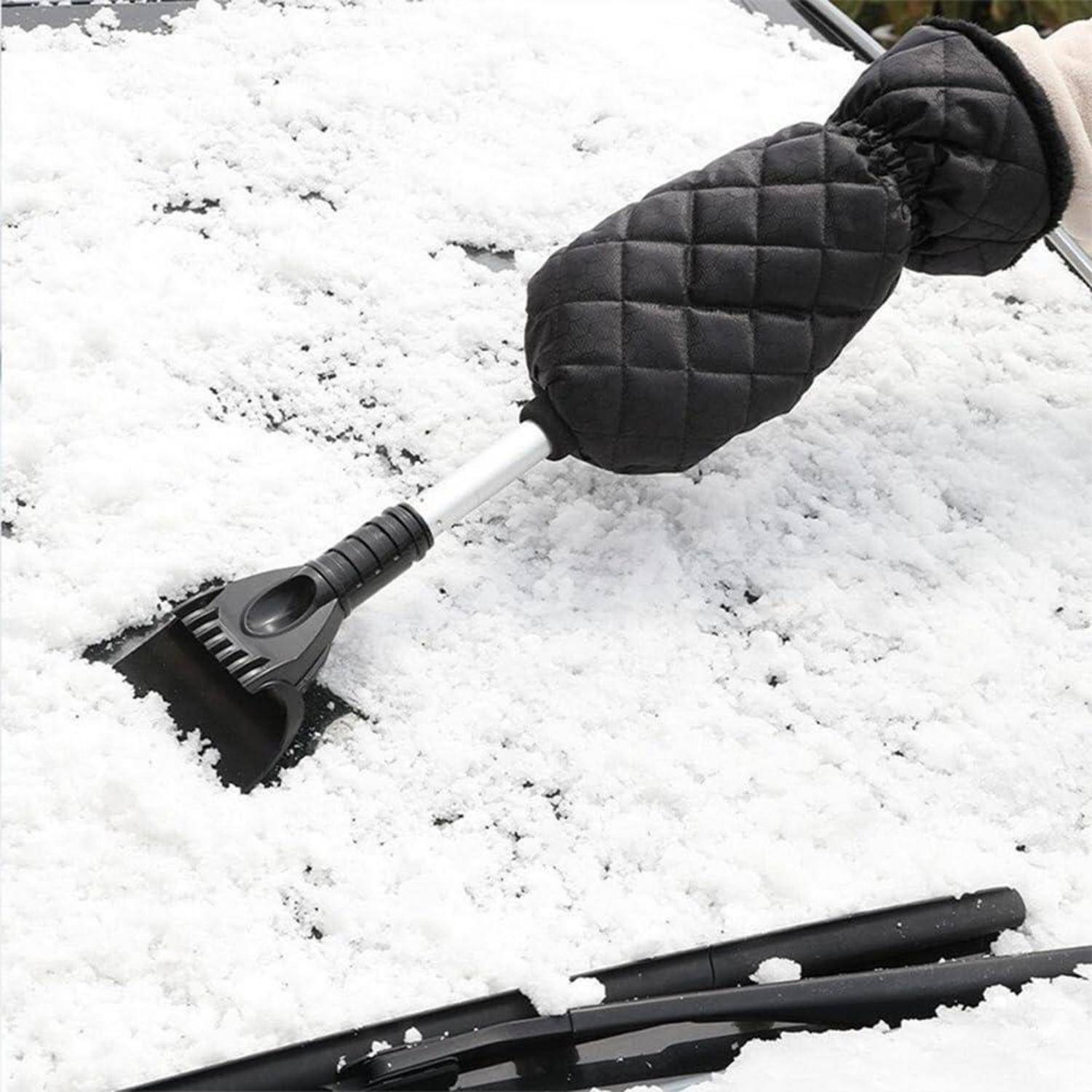 Behandschuhte Hand, die einen Eiskratzer verwendet, um Schnee von einer Autoscheibe zu entfernen, wobei Scheibenwischer sichtbar sind.