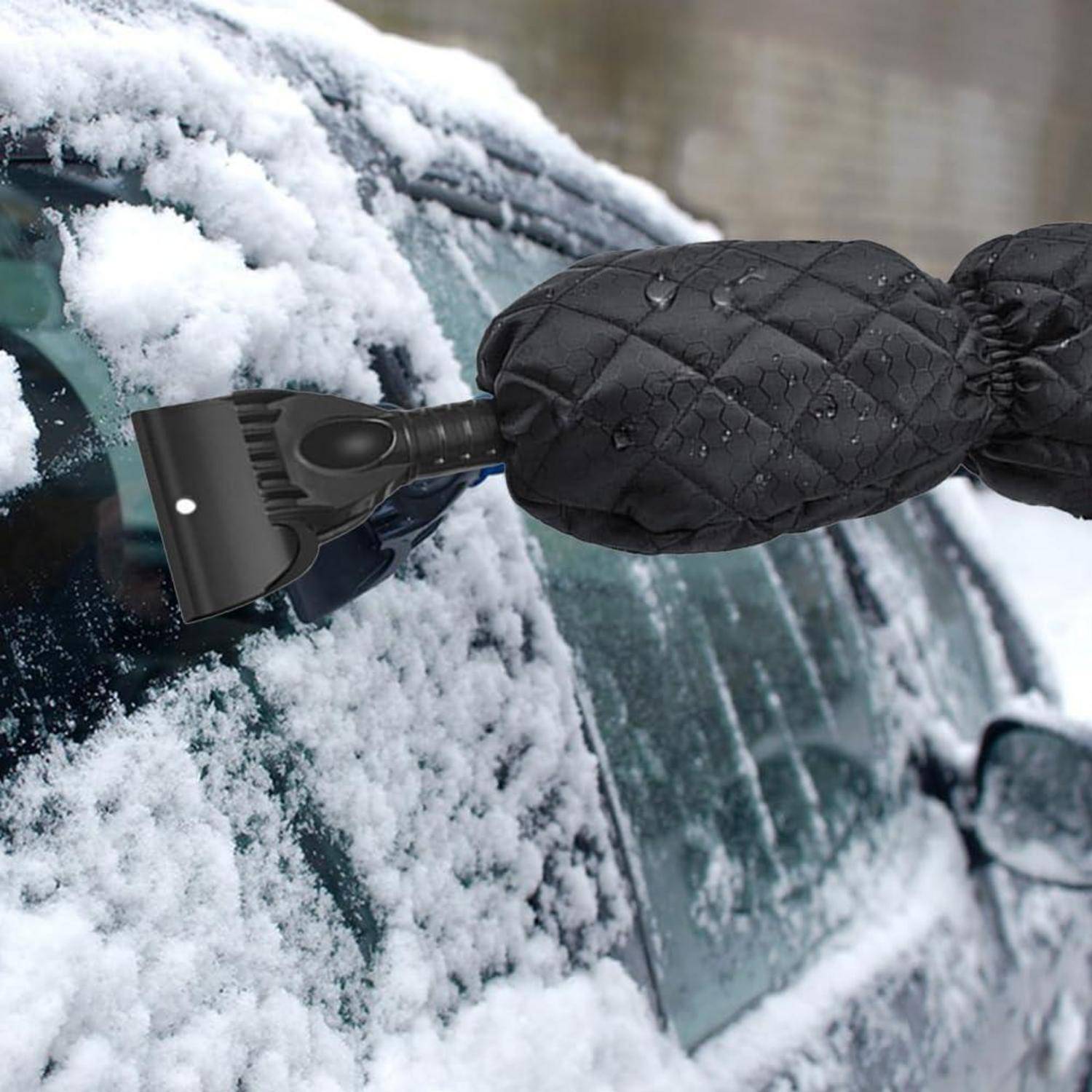Behandschuhte Hand, die Schnee und Eis mit einem Eiskratzer von einer Autoscheibe kratzt.