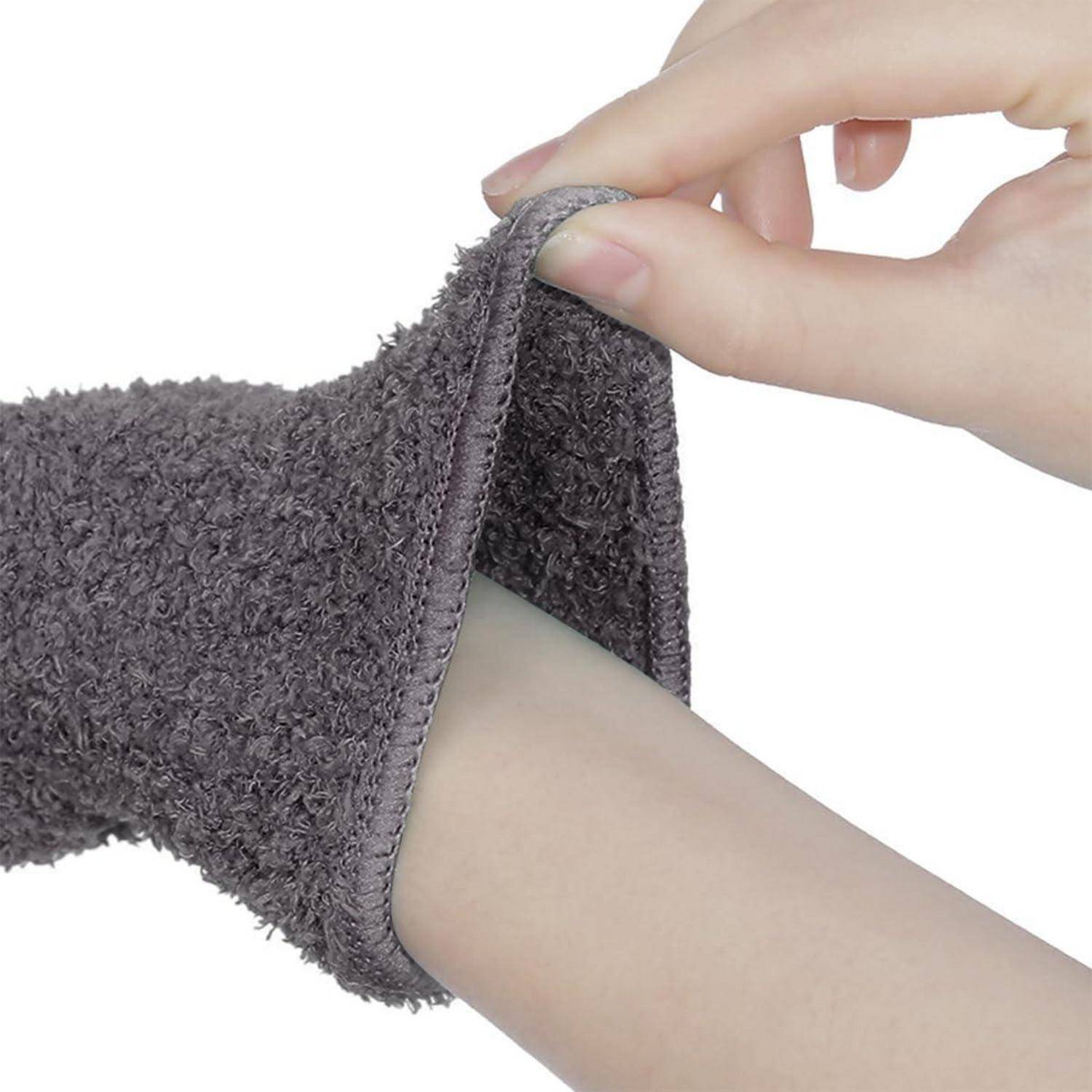 Nahaufnahme einer Hand, die einen grauen flauschigen Ärmel oder eine Socke über einen Fuß oder das Unterschenkel gegen einen weißen Hintergrund zieht.