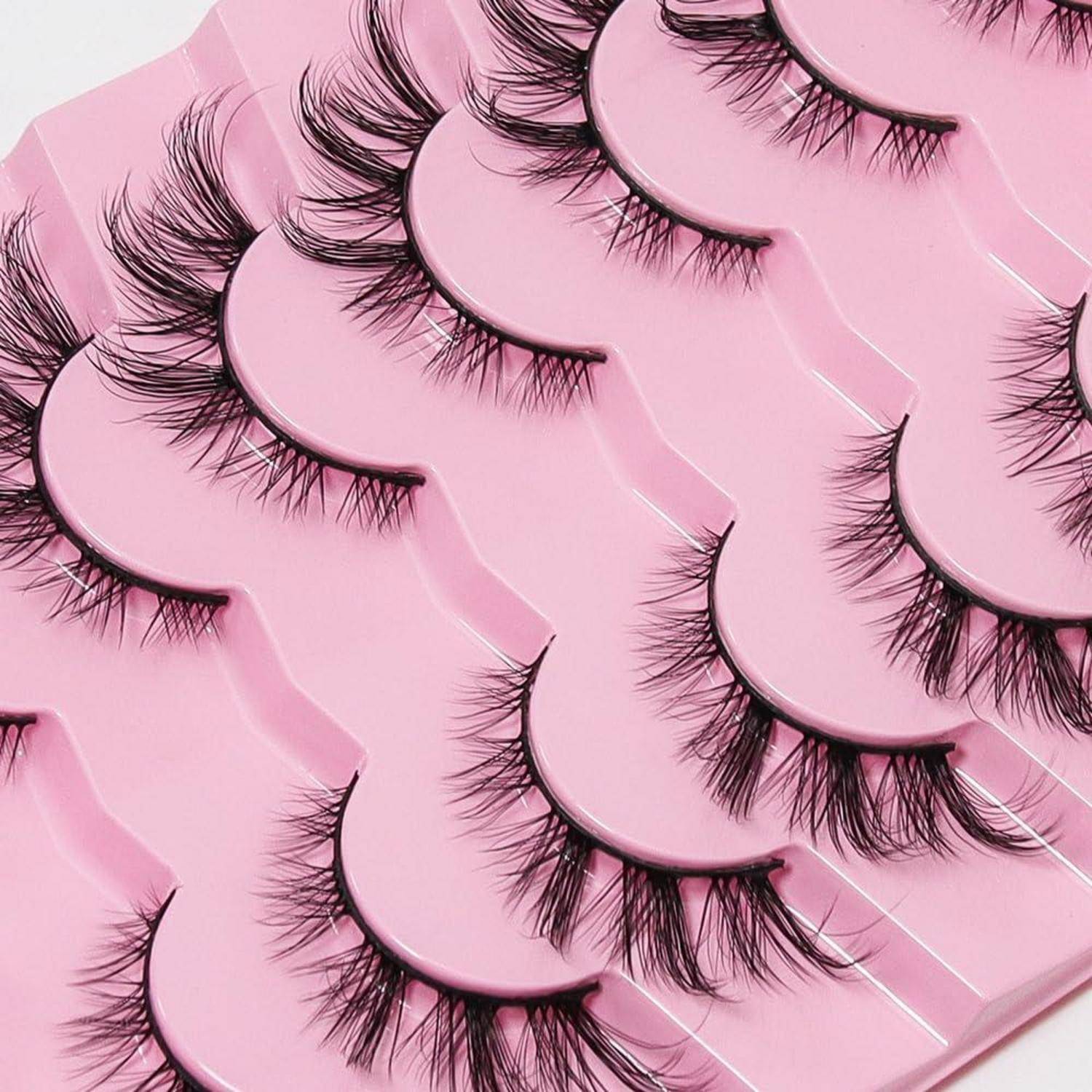Sortierte künstliche Wimpern in überlappenden rosa Kunststoffschalen, wahrscheinlich Produktverpackung für Schönheitskosmektika.