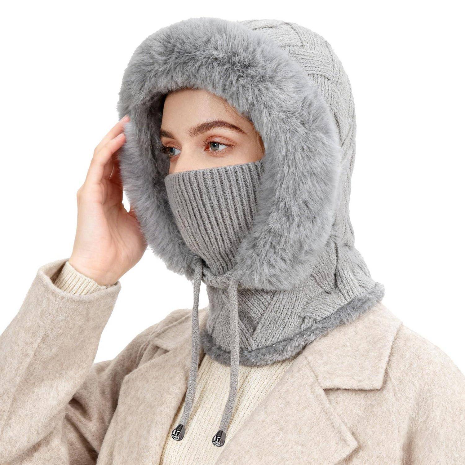 Person, die eine graue Winterkapuze mit Pelzbesatz, eine gestrickte Gesichtsabdeckung und einen beigen Mantel vor weißem Hintergrund trägt.