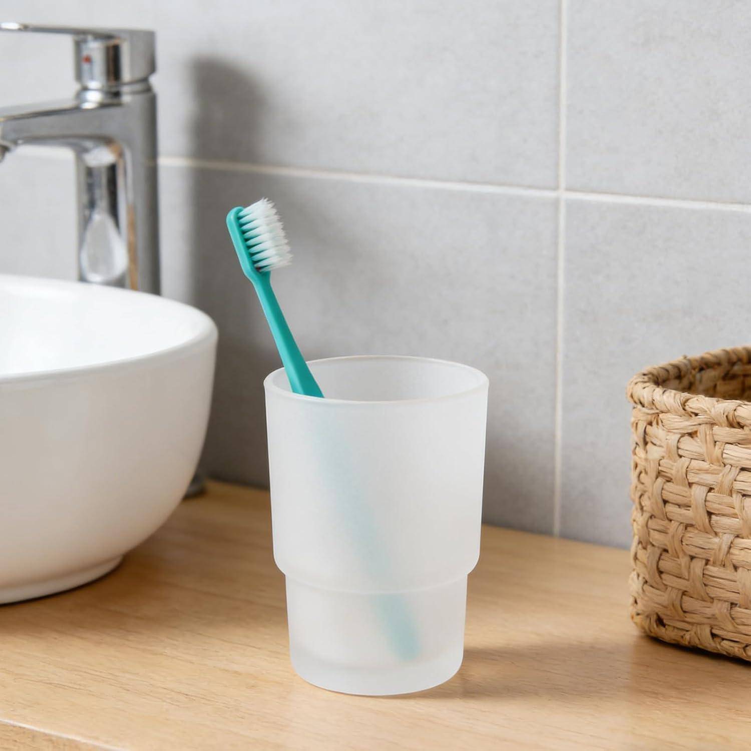 Zahnbürste in einem matter gefrosstetem Glas auf einer Badezimmer-Arbeitsplatte neben einem Waschbecken und einem Weidenkorb.