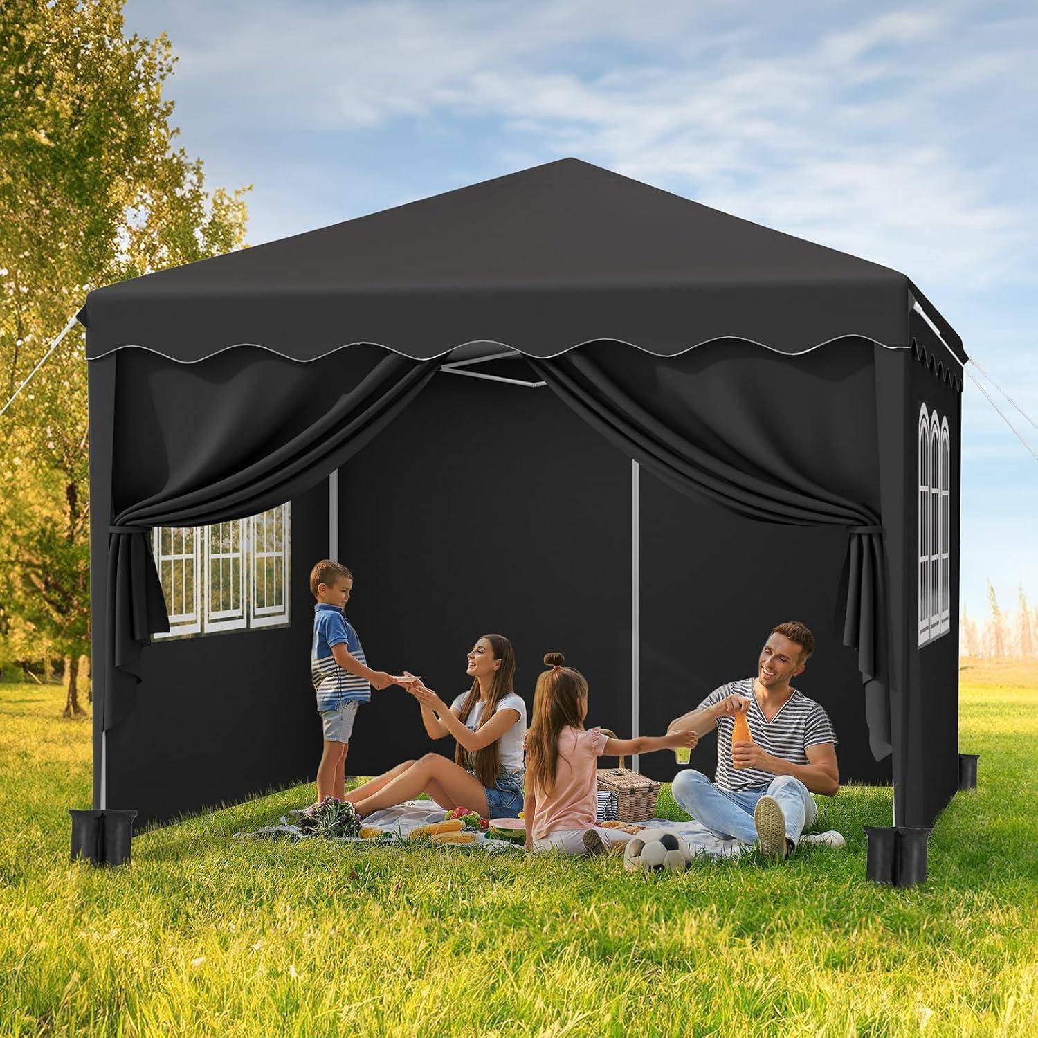 Eine Familie sitzt in einem schwarzen Outdoor-Pavillon-Zelt auf einer Wiese, wobei Erwachsene und Kinder entspannen und sich an den Händen halten.
