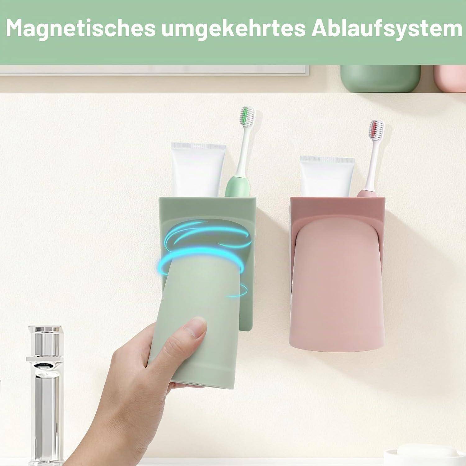 Zwei an der Wand montierte magnetische Zahnbürstenhalter halten Becher, Zahnpasta und Zahnbürsten; ein grüner Halter wird angehoben und zeigt ein reversibler Hängedesign.
