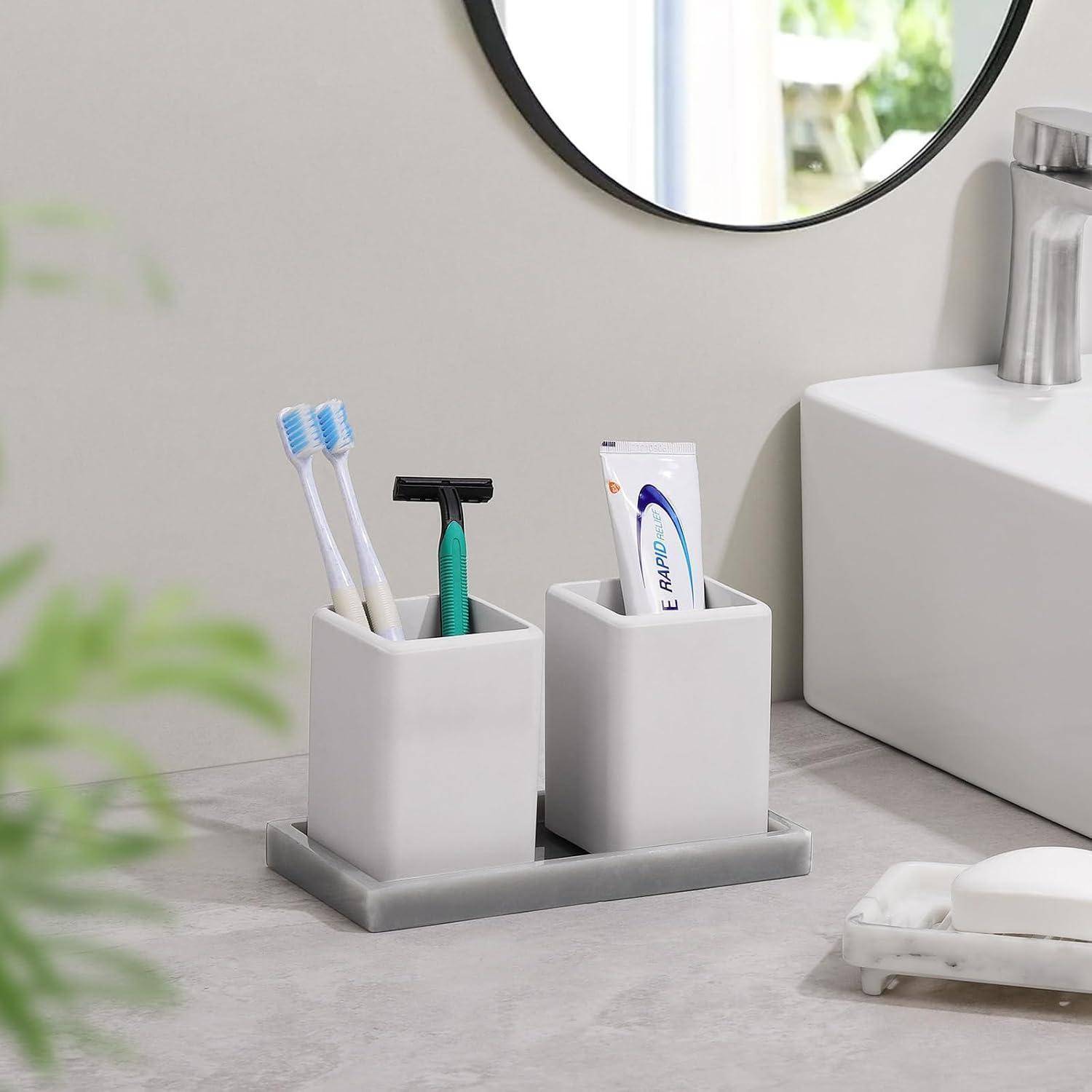 Badezimmer-Arbeitsflächenorganizer mit zwei weißen Behältern, die Zahnbürsten, einen Rasierer und Zahnpasta neben einem Waschbecken und einem Spiegel halten.
