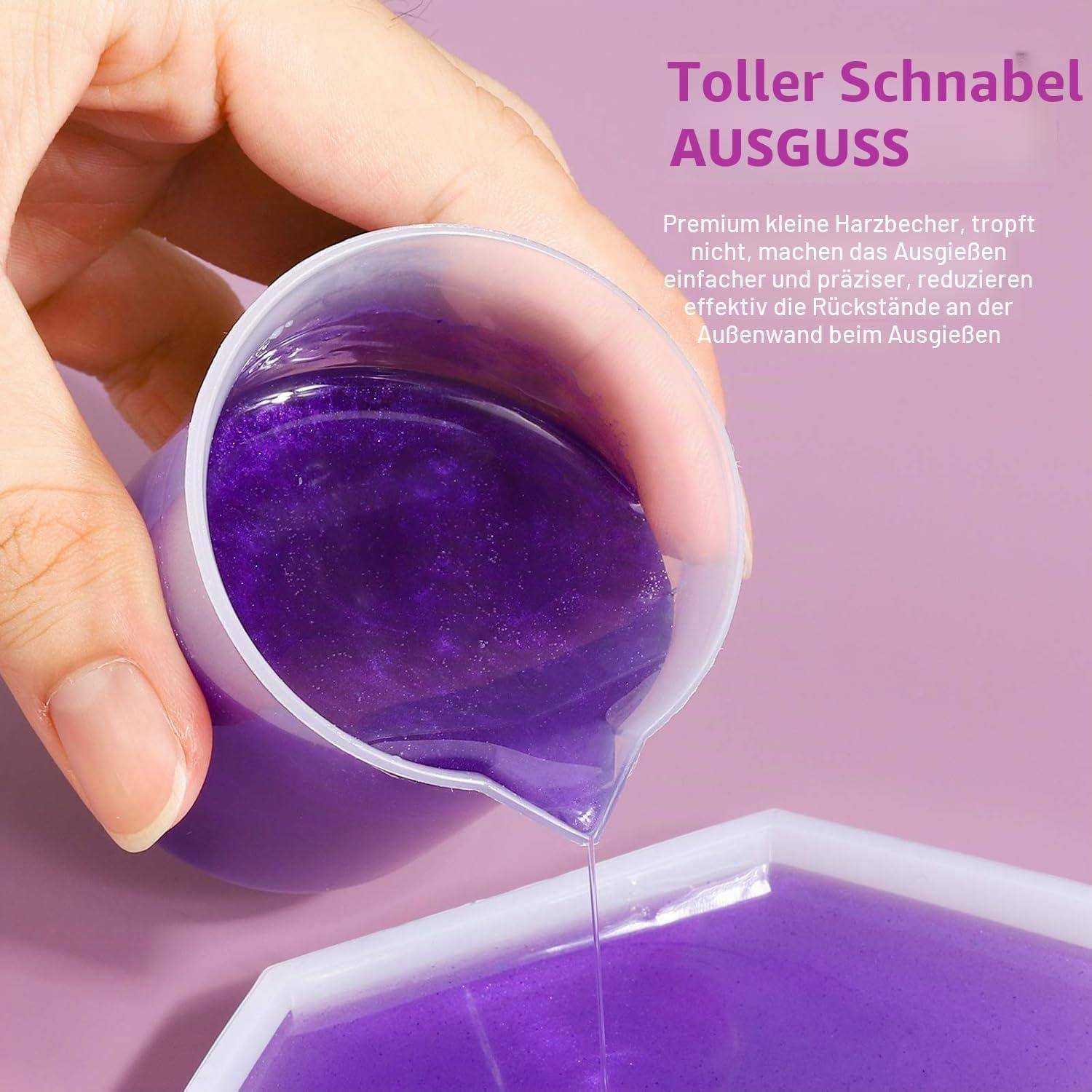 Eine Hand gießt violette Flüssigkeit aus einem kleinen Messbechner mit breitem Ausguss in einen Behälter; der Text sagt „Toller Schnabel AUSGUSS