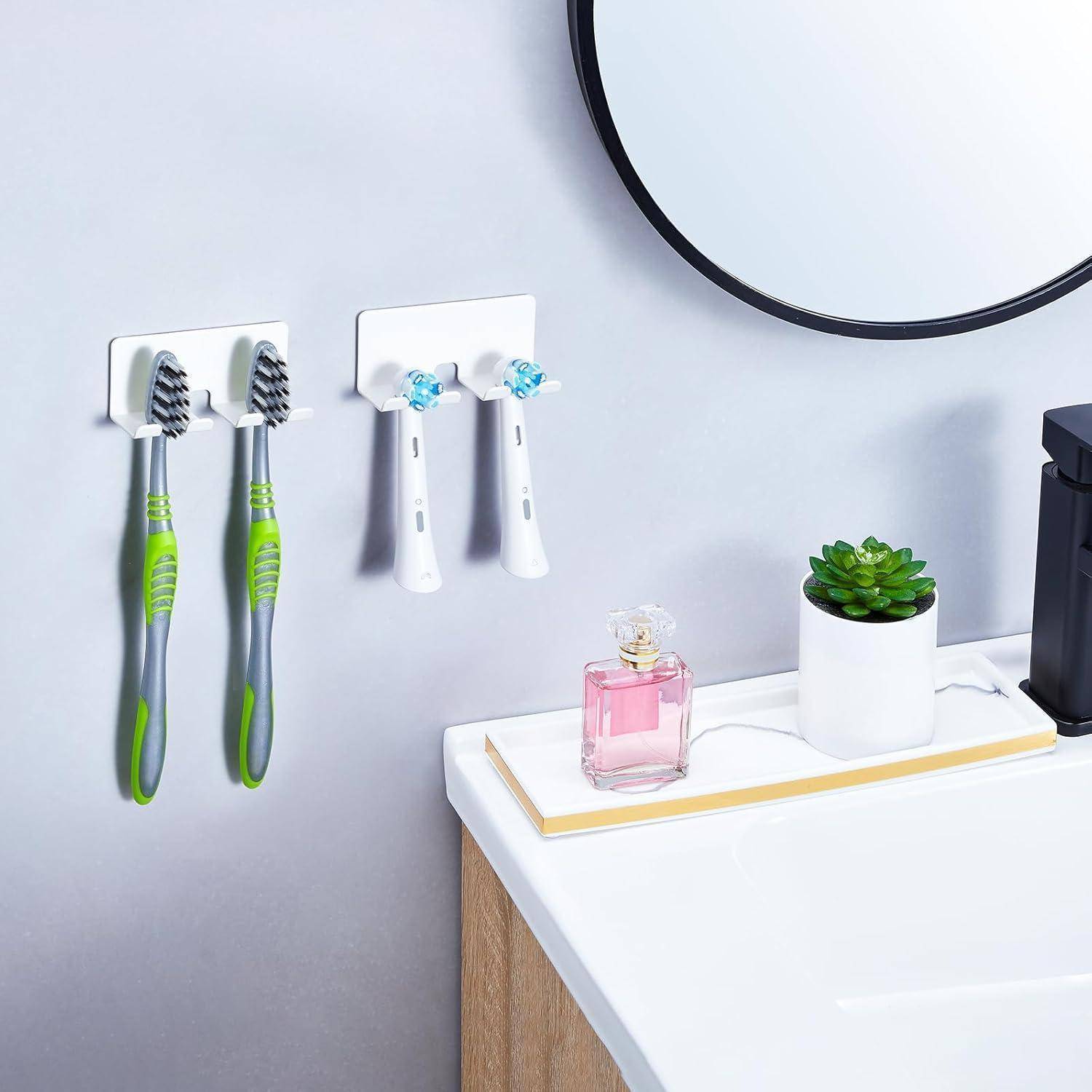 Badezimmerablage mit wandmontierten Haltern für zwei Zahnbürsten, einen Elektrorasierer und eine Zahnbürste, plus eine kleine Sukkulente und eine Parfümflasche neben einem Spiegel.