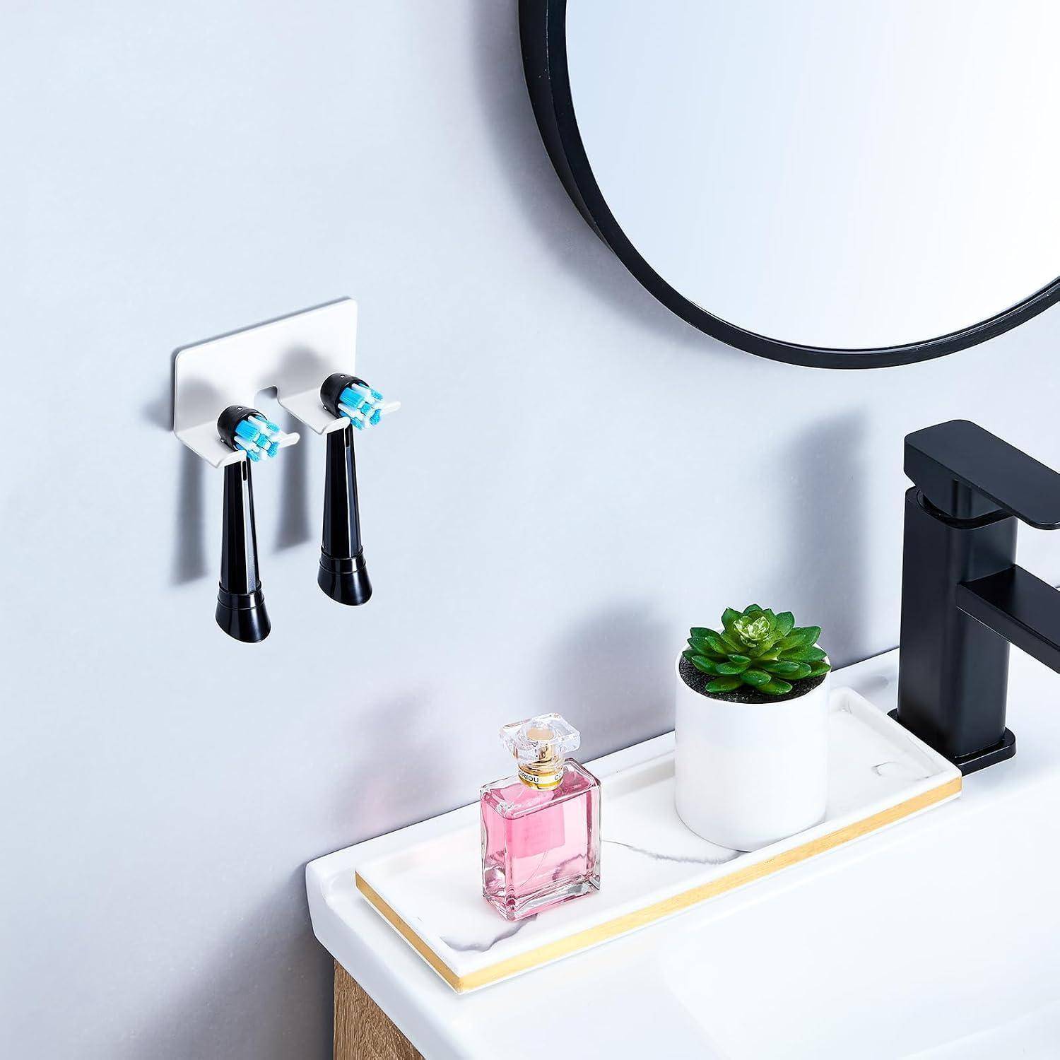 Modernes Badezimmerwaschtisch mit schwarzem Wasserhahn und rundem Spiegel; ein Tablett mit einer rosa Parfümflasche und einer kleinen Sukkulente neben einem an der Wand montierten Behälter für elektrische Zahnbürsten.