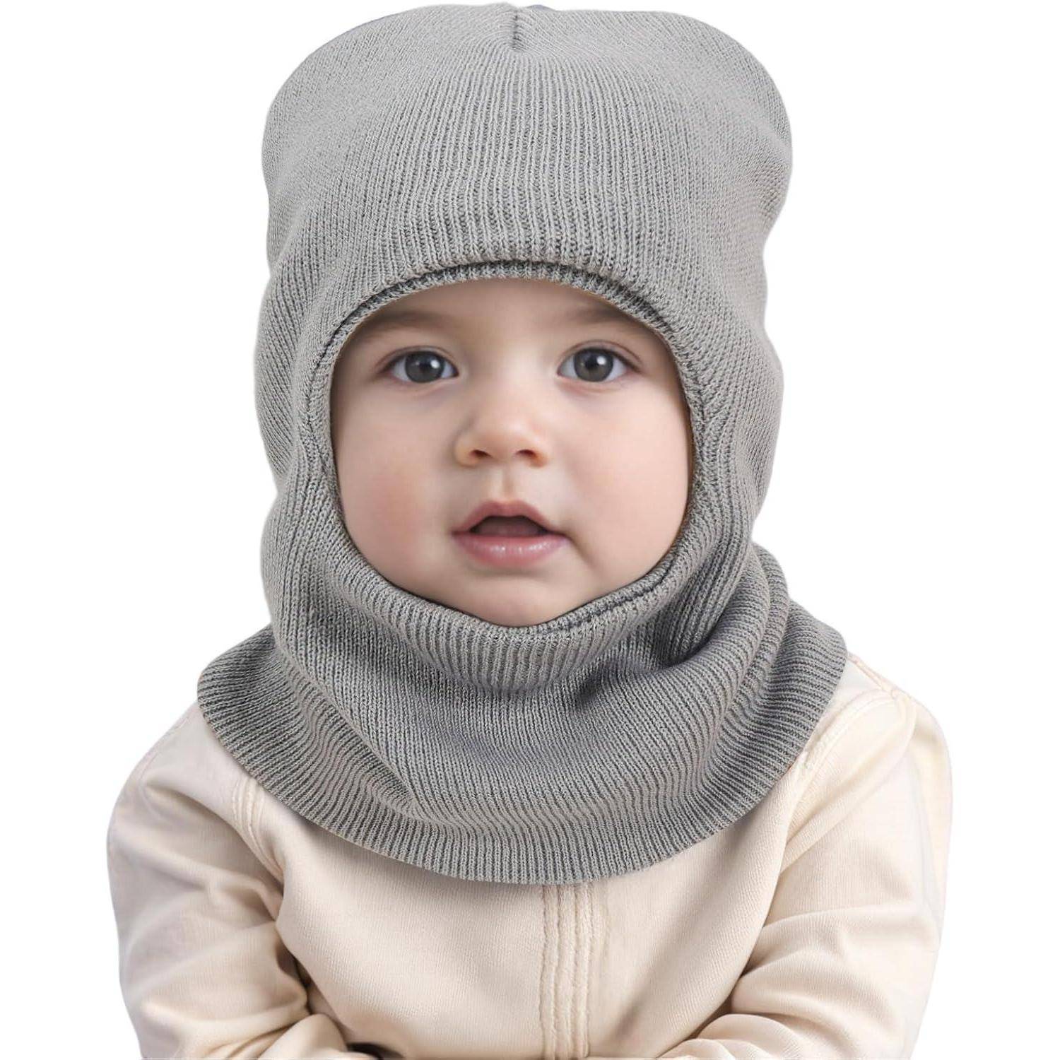 Nahaufnahme eines Babys, das eine graue gestrickte Sturmhaube mit Nackenwärmer trägt, wobei nur das Gesicht vor weißem Hintergrund sichtbar ist.