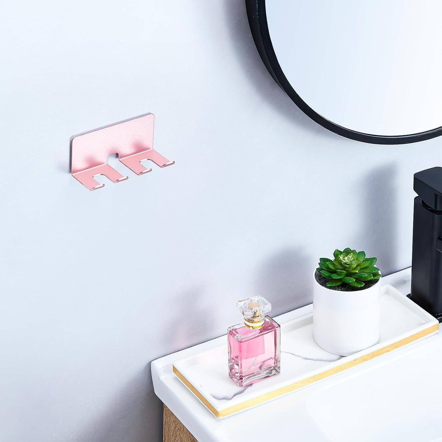 An der Wand montierter rosa Zahnbürstenhalter über einem Badezimmerregal mit Parfüm und einer Topfpflanze auf einem Tablett in der Nähe eines Spiegels.