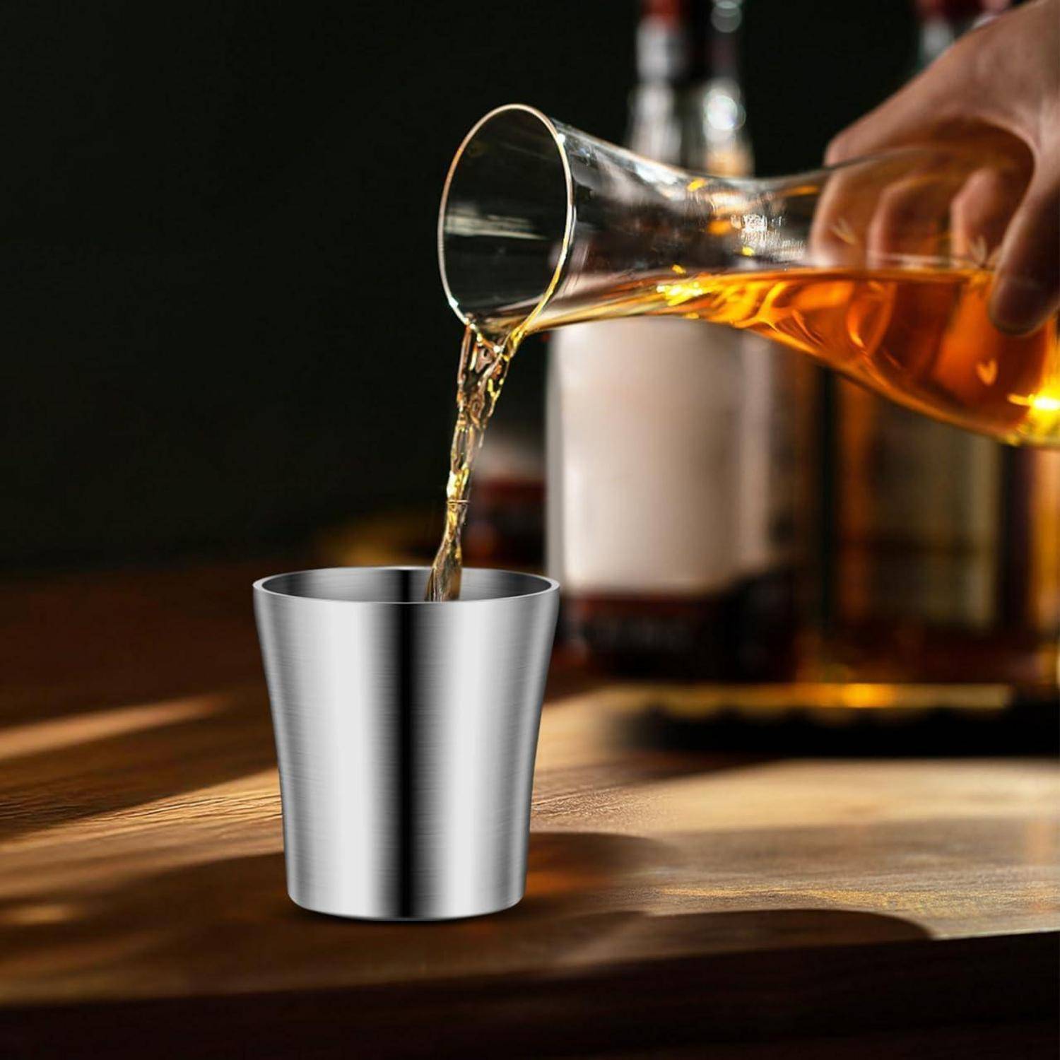 Whiskey wird aus einem Glaskaraff in einen Metallschnapsglas auf einem Holztisch gegossen.