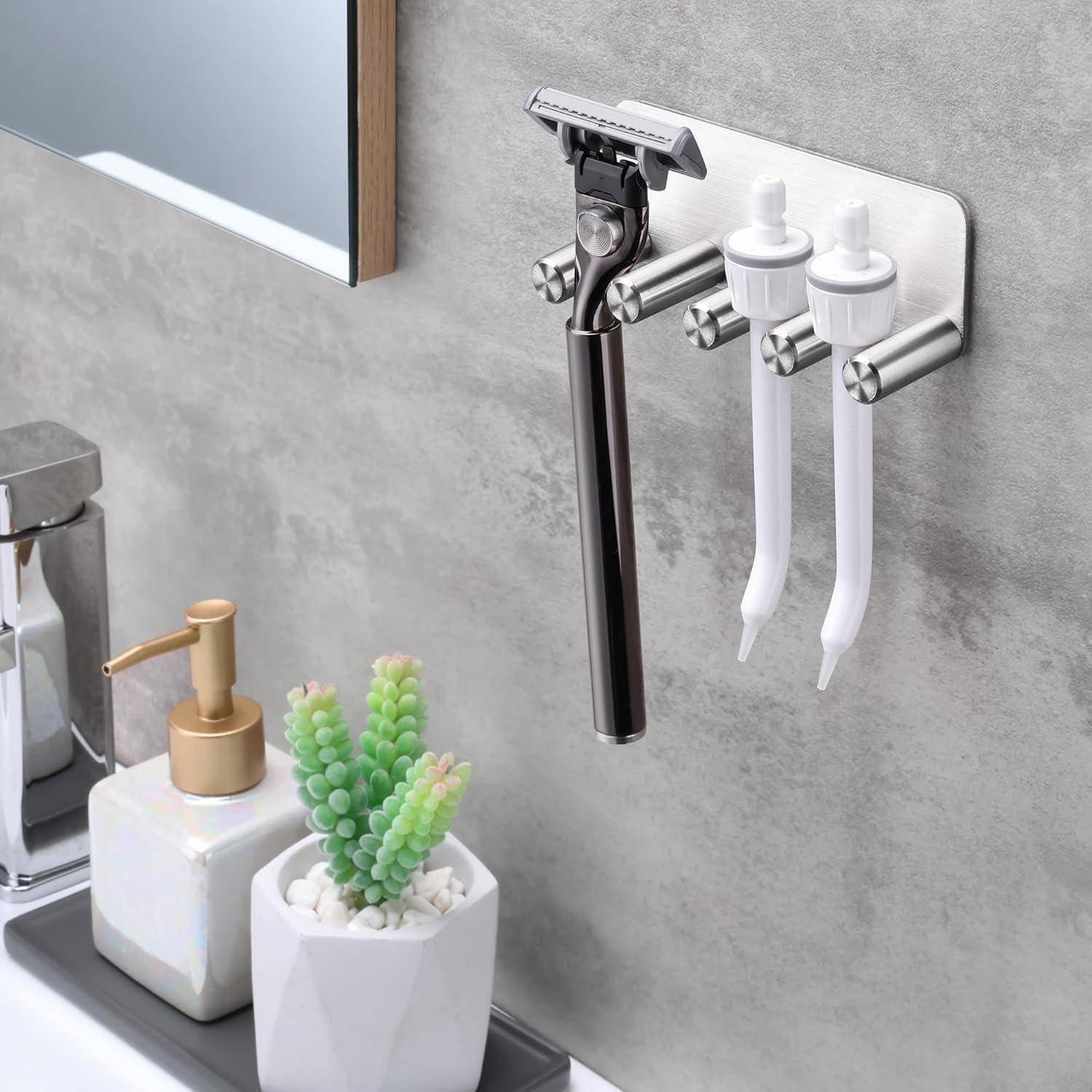 Wandmontierter Badezimmer-Rasiererhalter mit einem schwarzen Rasierer und zwei Zahnbürsten, die über einem Waschbecken angebracht sind, neben einem Seifenspender und einer kleinen Topfpflanze.
