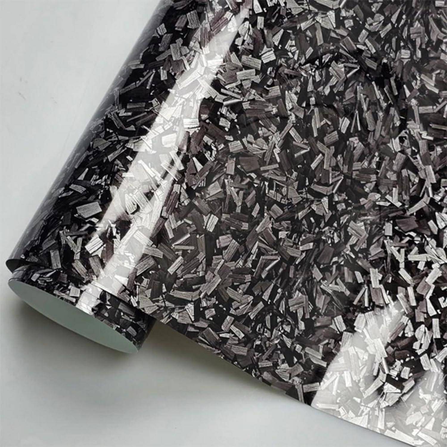 Nahaufnahme einer glänzenden schwarzen Rolle mit gemustertem Klebstofffilm mit weißen und grauen Flöckchen, teilweise auf hellem Hintergrund abgerollt.