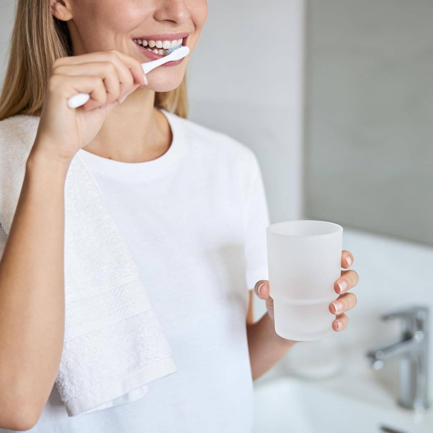Frau, die sich die Zähne putzt, während sie eine Tasse Wasser im Badezimmer hält.