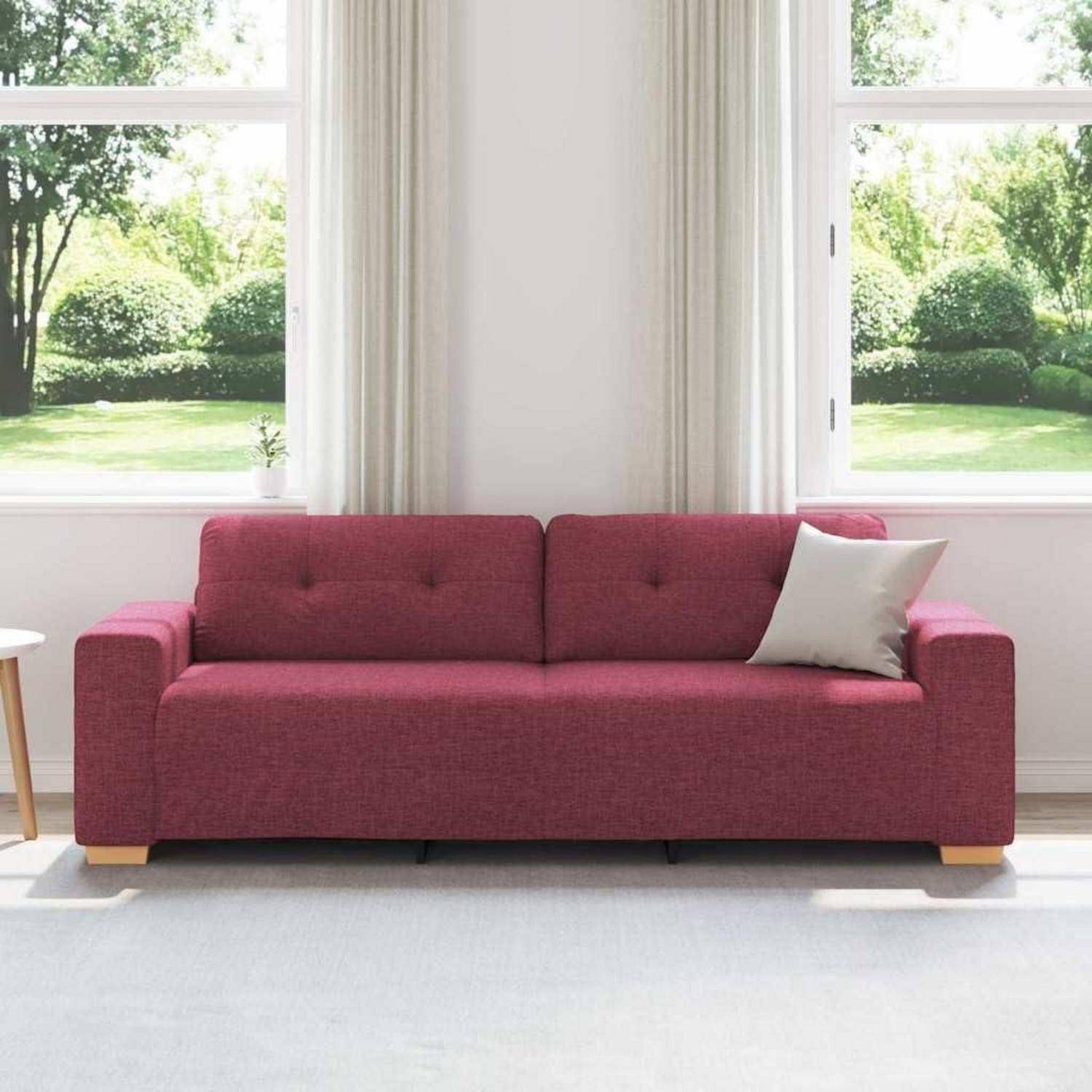 Magentafarbenes Polstersofa mit weißem Akzentkissen, zentriert zwischen zwei sonnigen Fenstern in einem hellen Wohnzimmer.