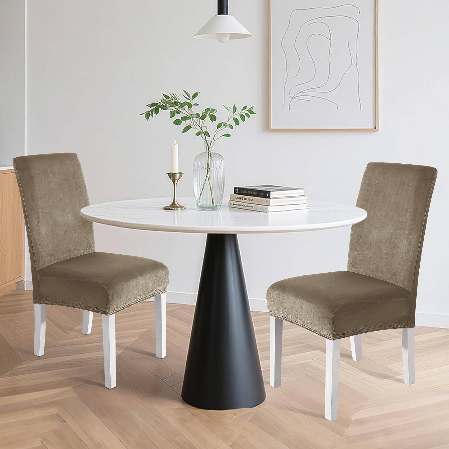 Moderner Essecke mit rundem weißem Tisch, zwei olivgrün gepolsterten Stühlen, Vase mit Grünpflanzen, Kerze, Büchern und minimalistischer Wandkunst.