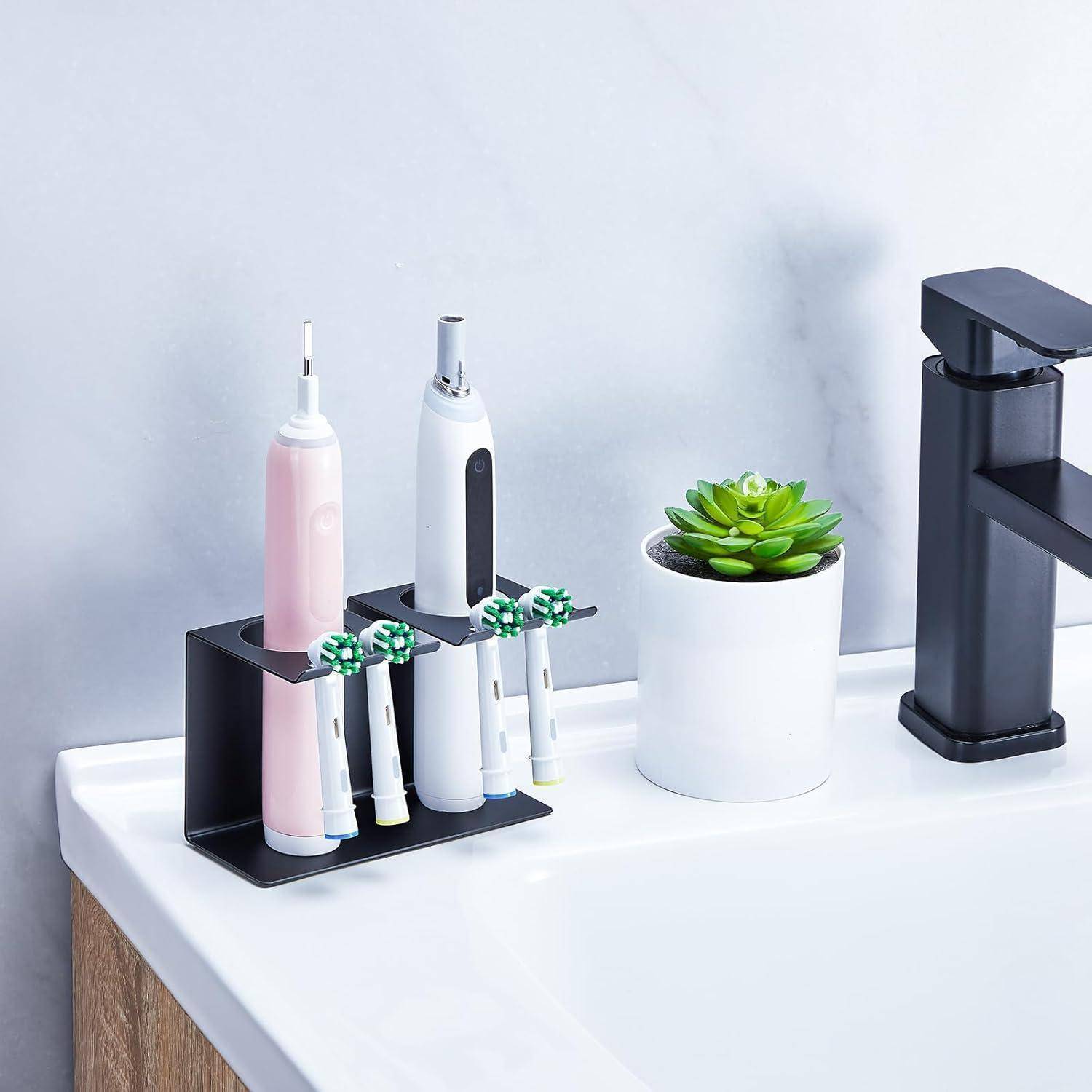 Badezimmerwaschtisch mit elektrischen Zahnbürsten in einem schwarzen Behälter, zwei Zahnbürstengriffe, eine kleine Topfpflanze mit Sukkulente und ein schwarzer Wasserhahn auf einer weißen Arbeitsplatte.
