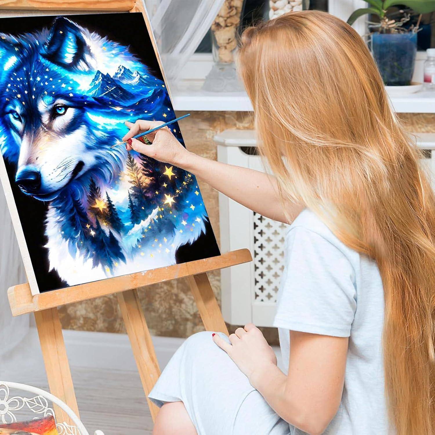 Eine Frau malt ein lebhaftes blaueszweites Wolfsporträt auf einer Staffelei in ihrem Heimstudio und verwendet einen Pinsel für detaillierte Kunstwerk.