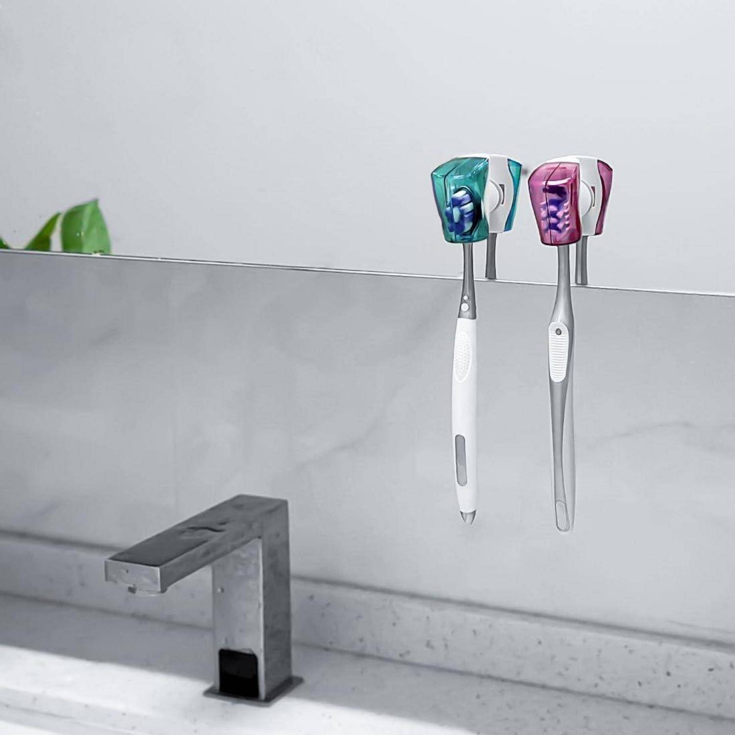 Zwei Zahnbürsten, die an wandmontiertem Zahnbürstenhalter über einem Badezimmerwasserhahn hängen.