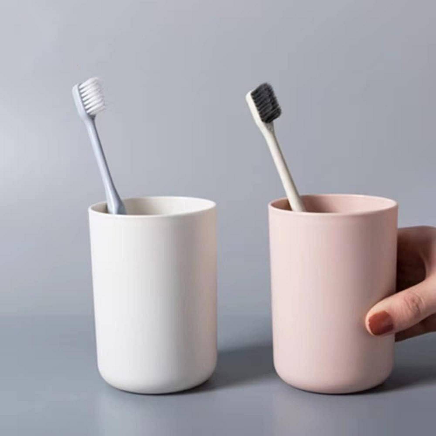 Zwei Zahnbürsten in minimalistischen Bechern, eine weiß und eine rosa, mit einer Hand, die den rosa Becher hält.