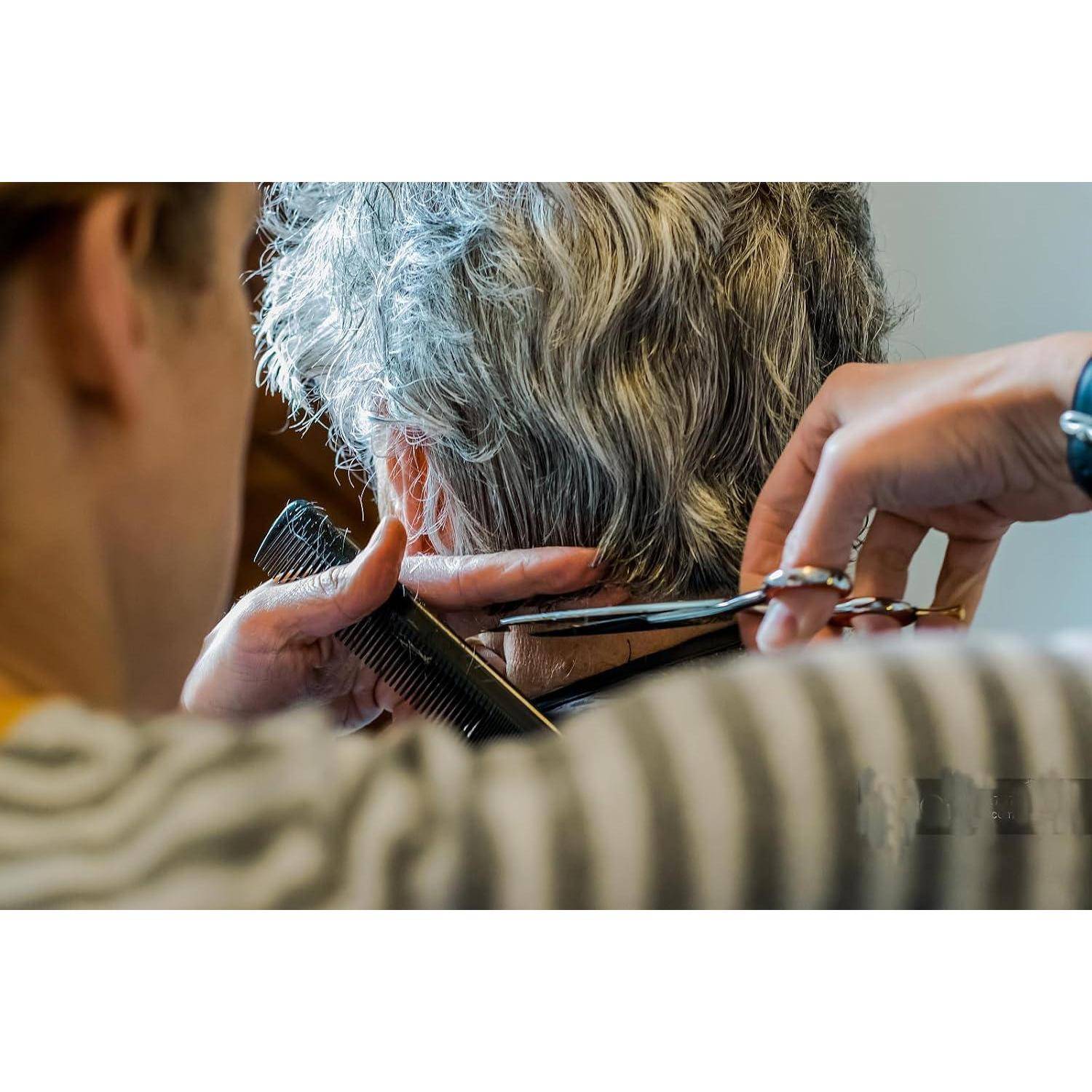 Nahaufnahme eines Friseurs, der einer älteren Person mit Schere und Kamm das kurze graue Haar im Salon schneidet.