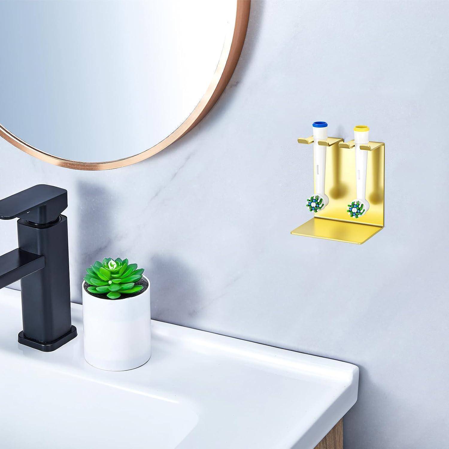 Badezimmerspüle mit schwarzem Wasserhahn, kleine getopfte Sukkulente und an der Wand montierter Zahnbürstenhalter aus Gold, der zwei Zahnbürsten hält.
