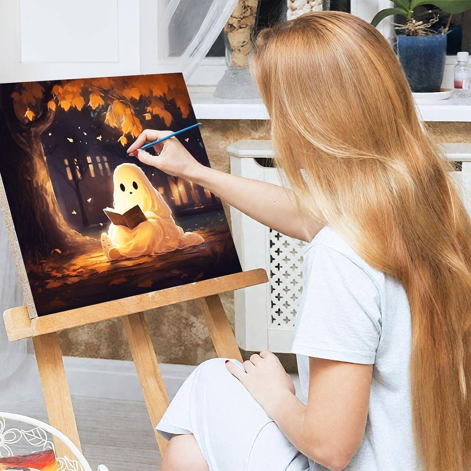Frau, die ein leuchtendes Gespenst malt, das auf einer Staffelei ein Buch liest, in einem Atelier, wobei sie mit einem Pinsel Details zu einer dunklen Herbstszene hinzufügt.