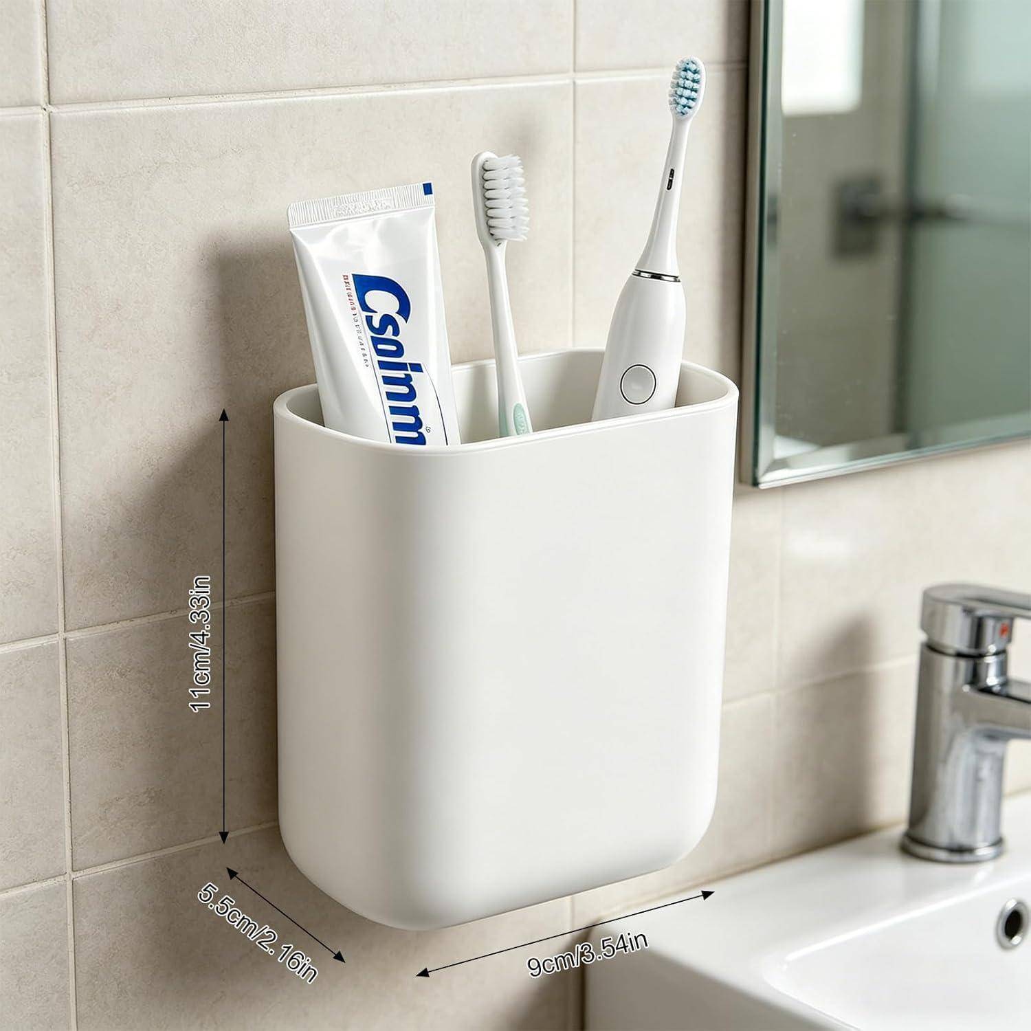 Weiße wandmontierte Badezimmerorganizer mit einer Zahnpastatube, einer manuellen Zahnbürste und einer elektrischen Zahnbürste neben einem Waschbecken; Abmessungen angegeben: 11 cm hoch, 6,5 cm tief, 9 cm breit.