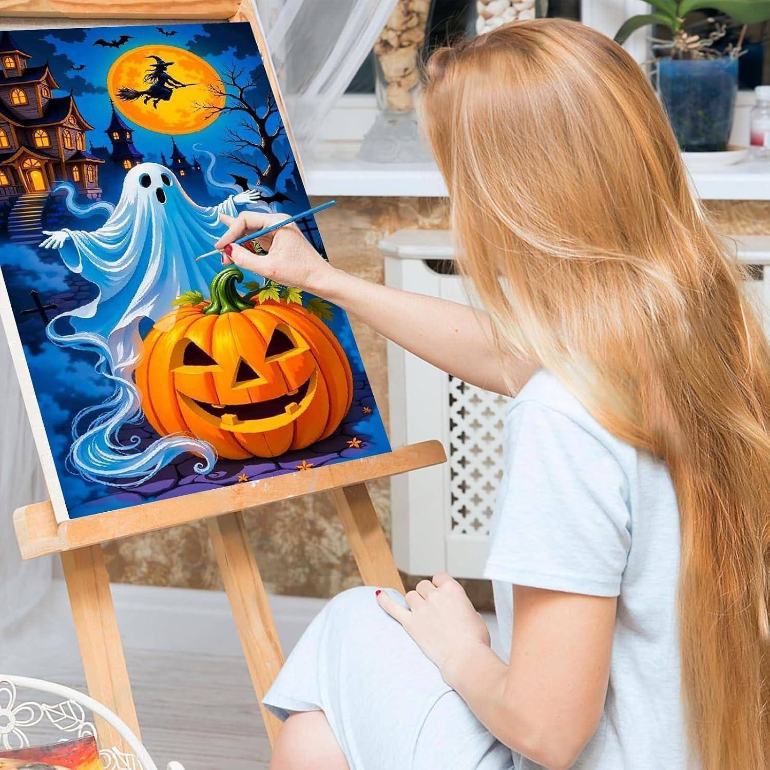 Eine Frau malt eine Halloween-Szene mit einem Gespenst und einem Kürbis-Fratzengesicht auf einer Staffelei, mit einem Spukhaus und einem mondbeleuchteten Himmel im Hintergrund.