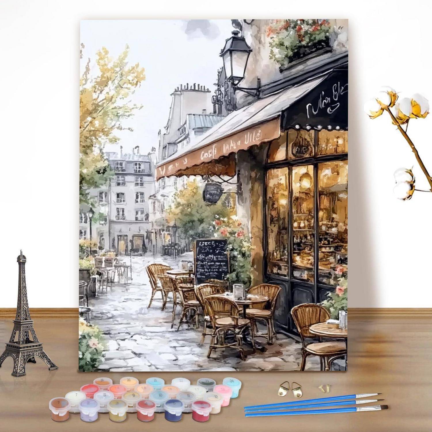 Kunstbedarf arrangiert um ein Aquarellgemälde einer Pariser Caféstraße mit Außentischen, Stühlen und dem Eiffelturm in der Ferne herum.