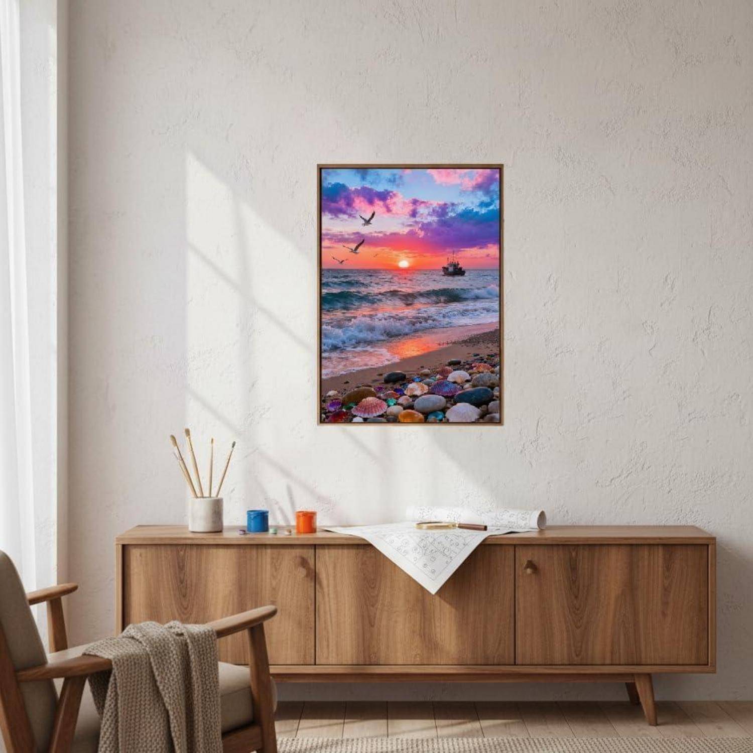 Minimalistisches Wohnzimmer mit Holzkommode unter einem gerahmten Druck eines Sonnenuntergangs am Strand, sowie einem Stuhl und kleinen Dekorationsgegenständen auf dem Schrank.