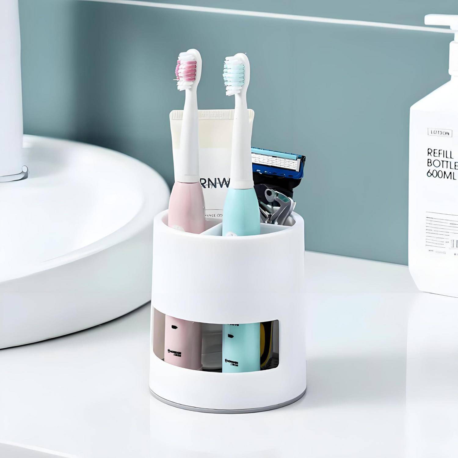 Weiße Badezimmer-Arbeitsplatte-Caddy mit zwei elektrischen Zahnbürsten, einem Rasierer und kleinen Toilettenartikeln neben einem Waschbecken und einer Nachfüllflasche.