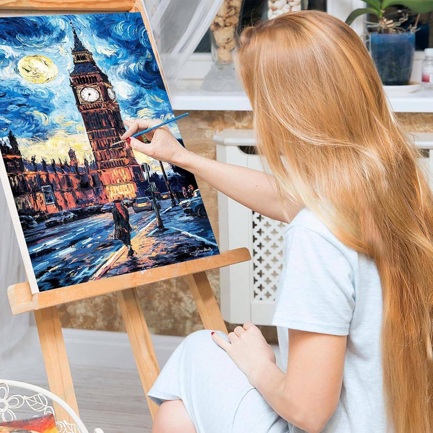 Eine junge Frau malt eine bunte Stadtlandschaft von Big Ben auf einer Staffelei in einem hellen Raum.
