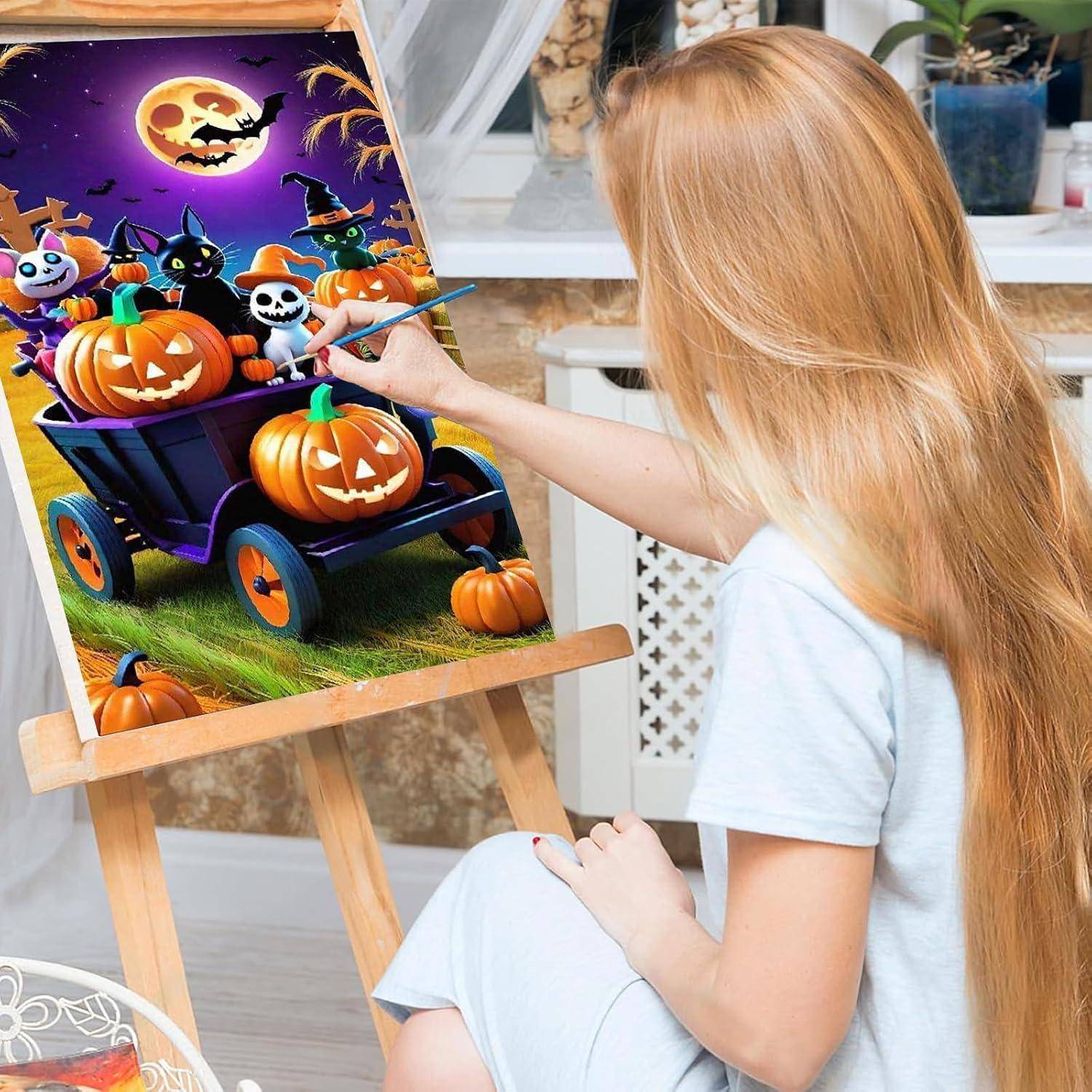 Eine junge Frau malt eine Halloween-Szene auf einer Staffelei und fügt Details zu einem kürbisbeladenen Wagen mit Fledermäusen, Schädeln und einem mondbeglänzten Himmel hinzu.