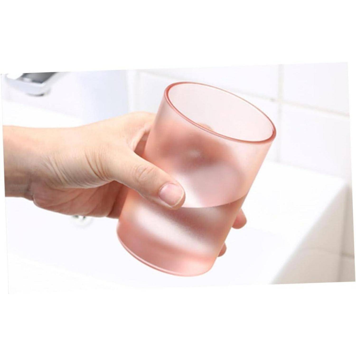 Eine Hand hält ein mattiertes, rosa durchscheinendes Trinkglas über einem Spülbecken oder einer Arbeitsplatte.