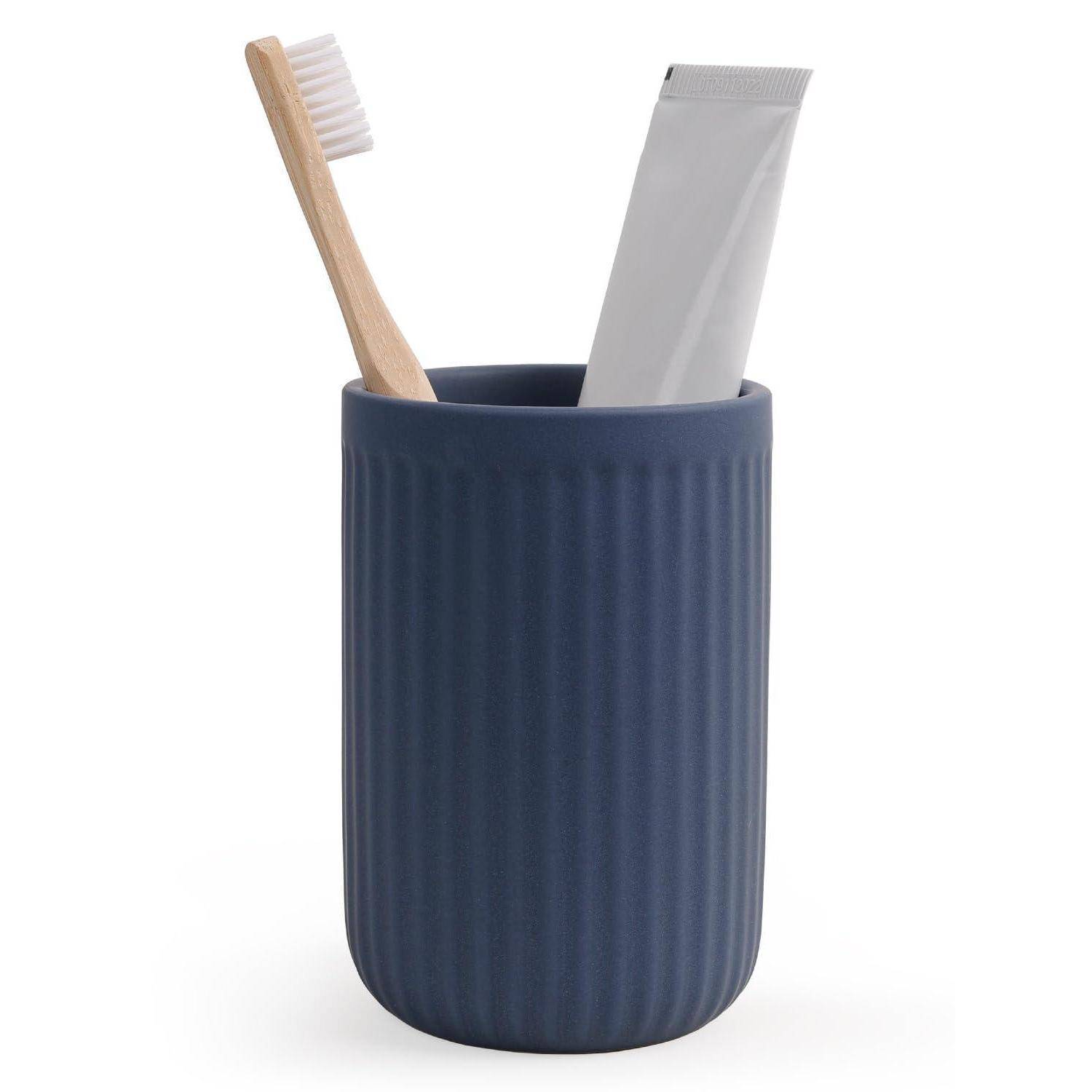 Blaue gerippte Badezimmertasse mit Zahnbürste und Zahnpastatube auf weißem Hintergrund.
