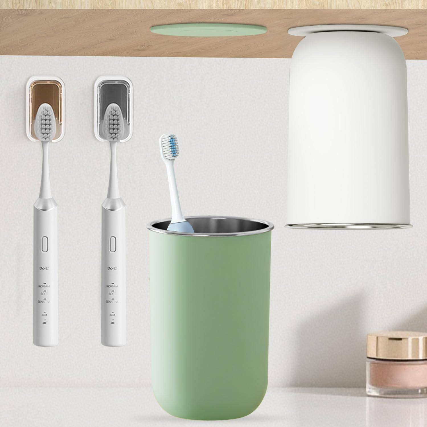 Zwei elektrische Zahnbürsten in wandmontierten Haltern neben einer grünen Tasse mit einer Zahnbürste und einem weiß wandmontierten Behälter oben auf einem Badezimmerregal.
