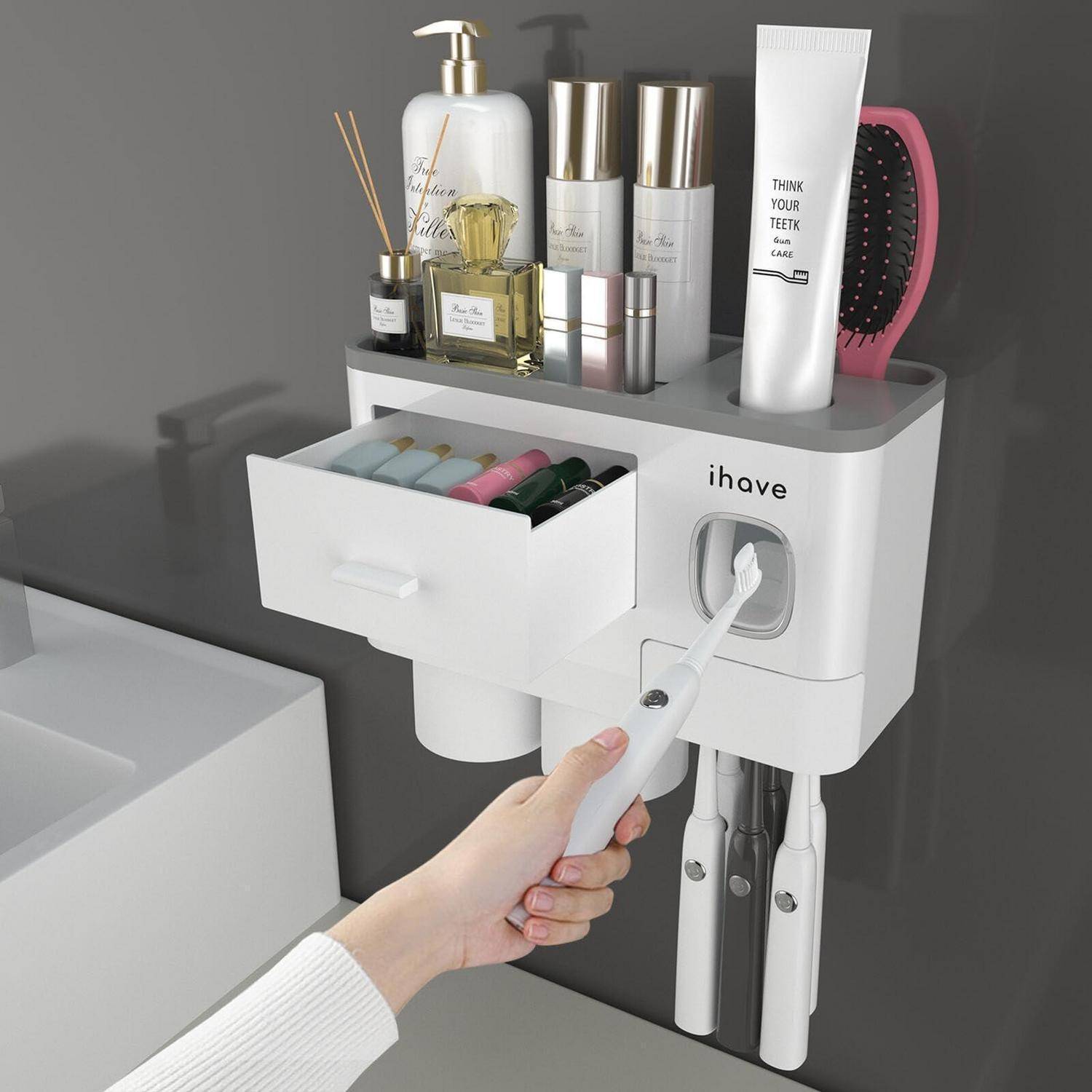 An der Wand montierter Zahnbürstenorganizer und Regal mit Schublade, Zahnpastatube, elektrische Zahnbürsten und Pflegeartikel; eine Hand führt eine Zahnbürste ein