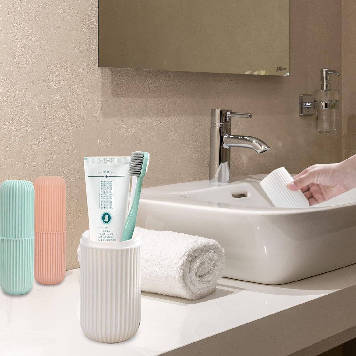 Badezimmerschrank mit Waschbecken und chromglänzendem Wasserhahn; eine Hand hält eine weiße Tasse in der Nähe des Beckens, mit Zahnbürste, Zahnpasta, Handtüchern und pastellfarbenen Behältern auf der Arbeitsplatte.