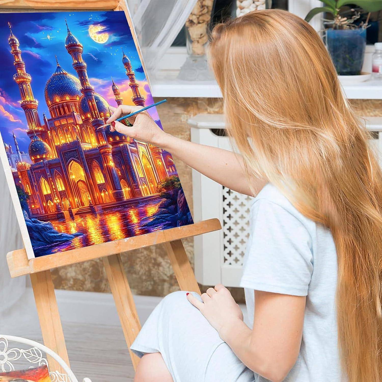 Eine Frau malt eine farbenfrohe Nachtszene einer Moschee auf einer Staffelei in einem Atelier.