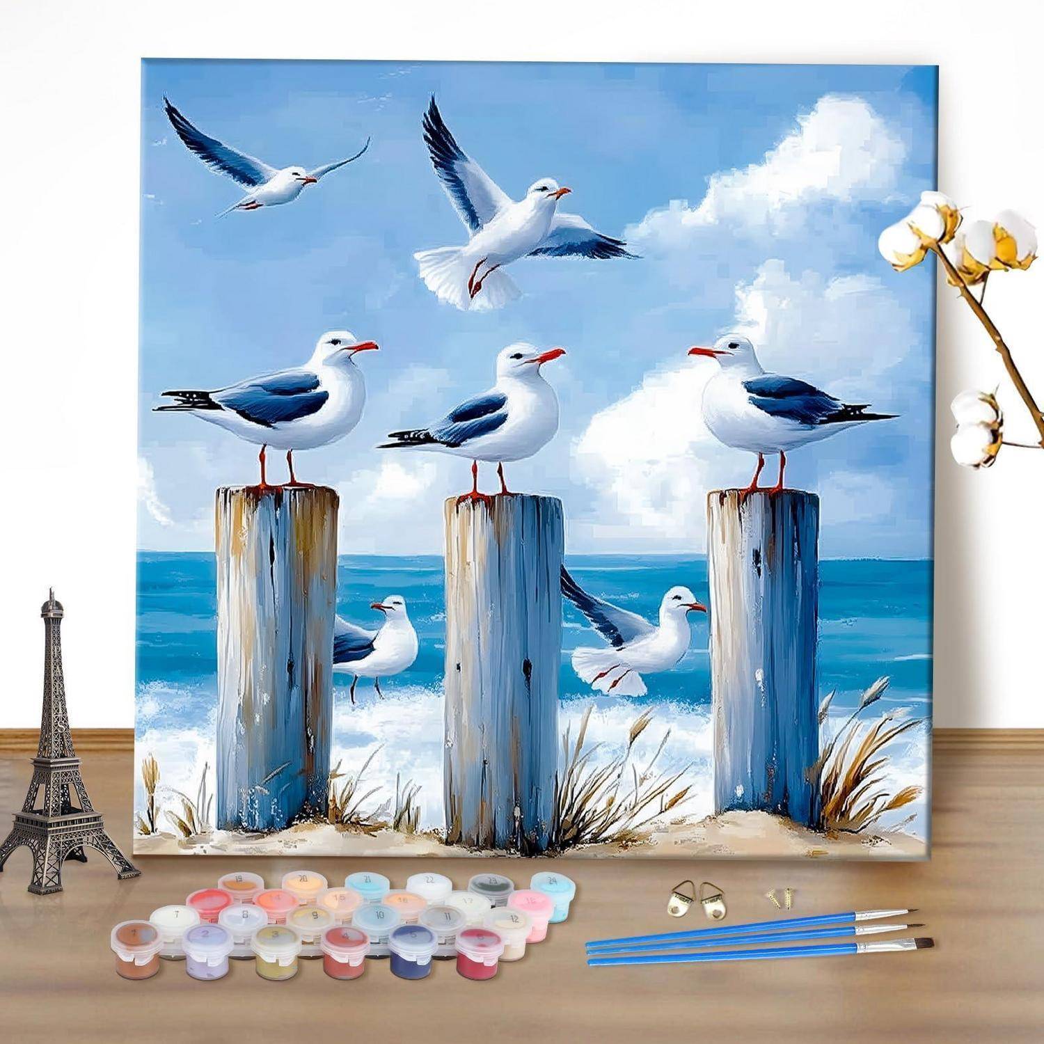 Malen-nach-Zahlen-Leinwand mit Möwen auf Holzpfosten über dem Meer, mit Farben und Pinseln, die unten ausgelegt sind.