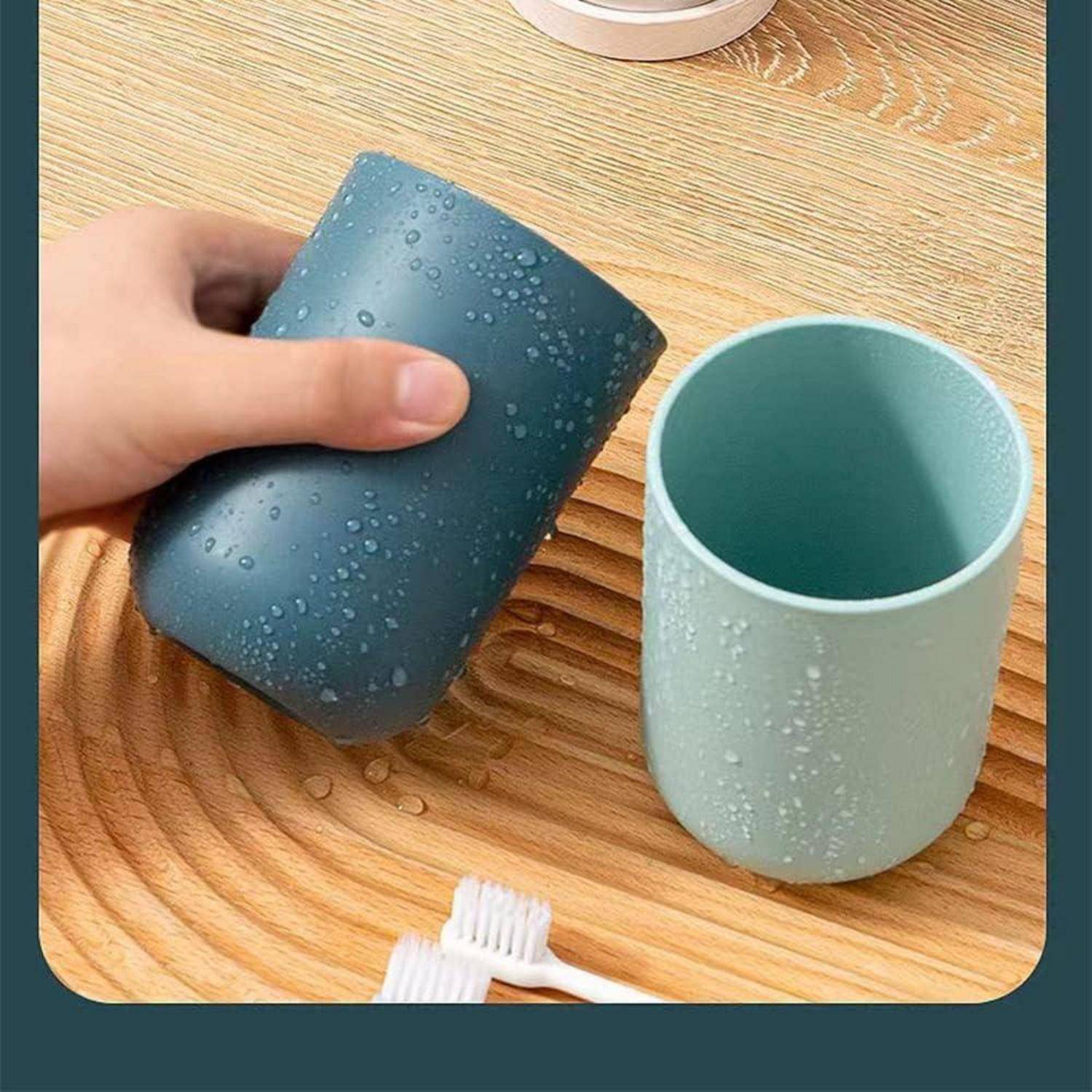 Eine Hand hält eine blaue Tasse mit Wassertropfen-Textur neben einer passenden hellgrünen Tasse auf einer Holzoberfläche.