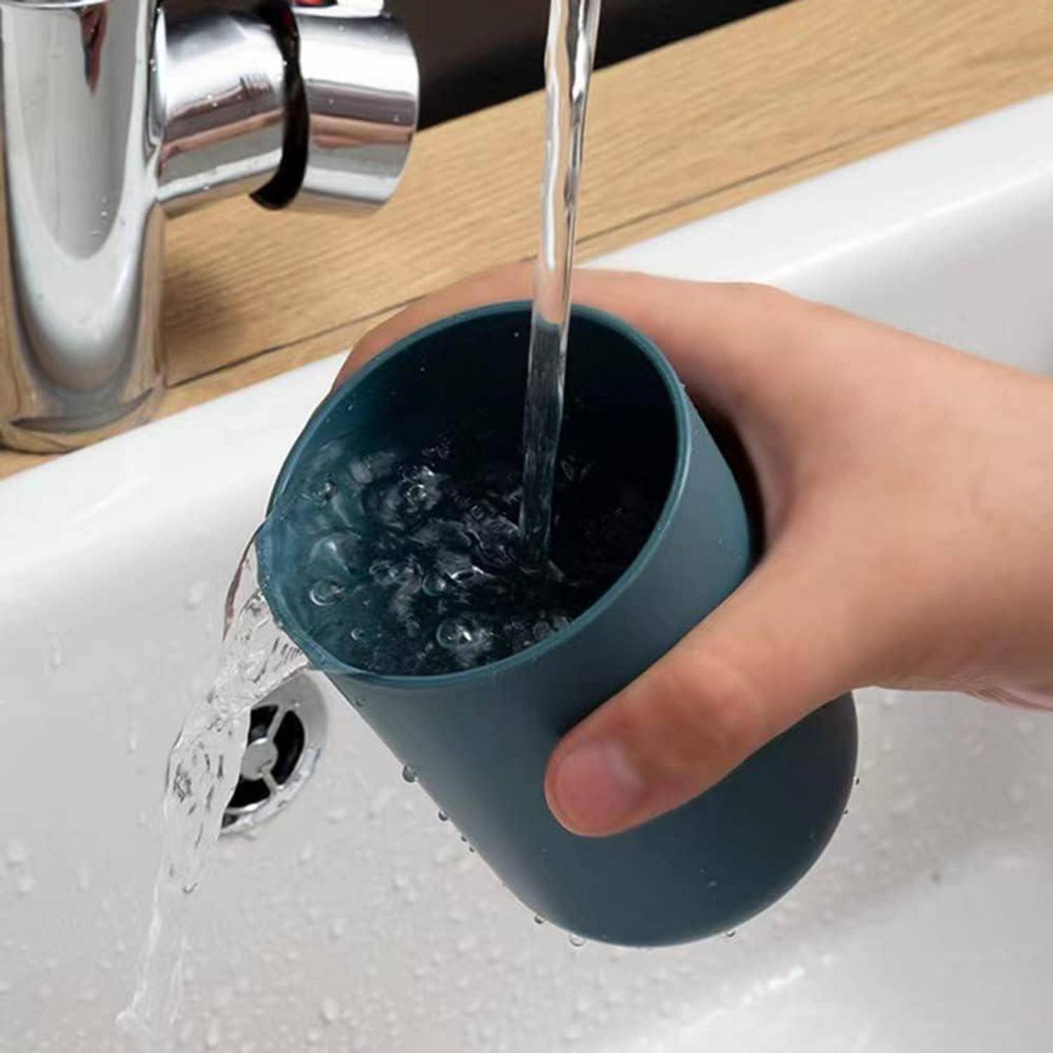Eine Hand spült eine blaue Tasse unter einem laufenden Wasserhahn in einem Küchenbecken.