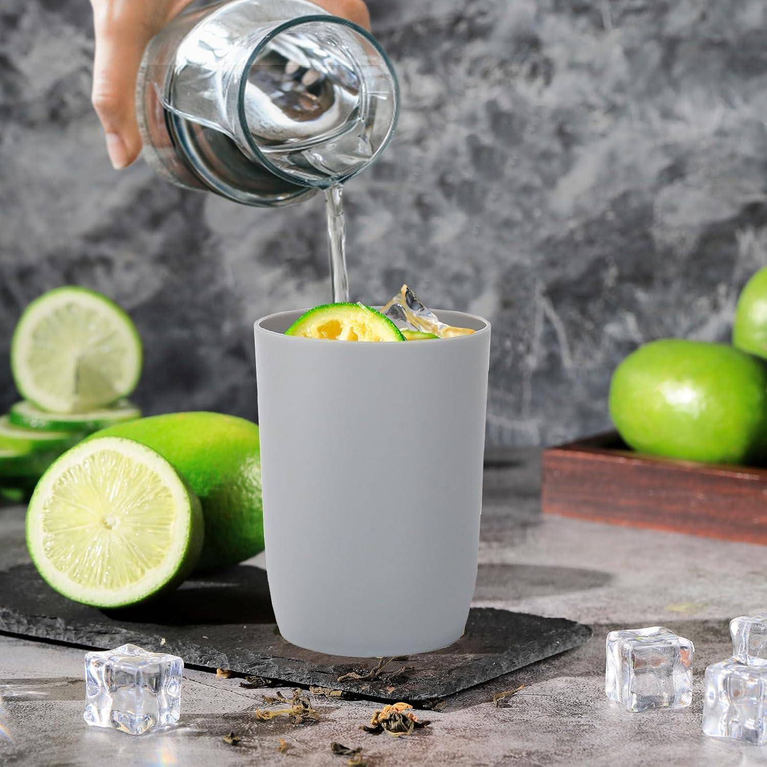Eine Hand gießt klare Flüssigkeit in eine graue Tasse mit Limettenscheiben, Eis und Minze, umgeben von ganzen und geschnittenen Limetten auf einer Steinoberfläche.