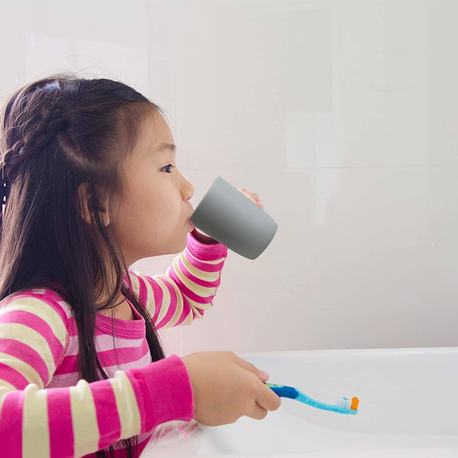 Junges Kind putzt sich im Badezimmer die Zähne, während es aus einer Tasse trinkt, und zeigt die Zahnputz-Hygiene-Routine.